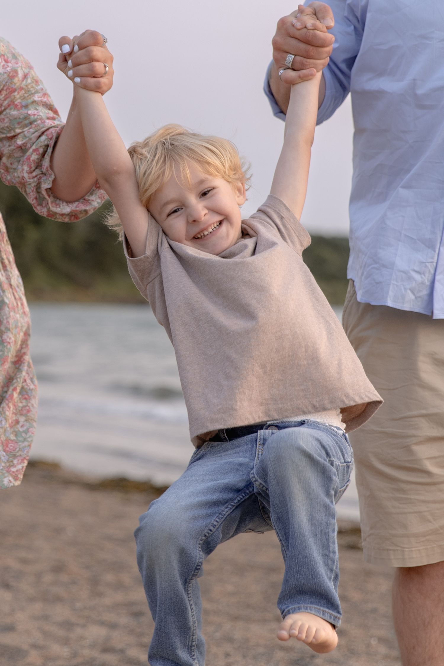 Joyful playtime moments on the beach as someone swings a child while their feet dangle in the air.