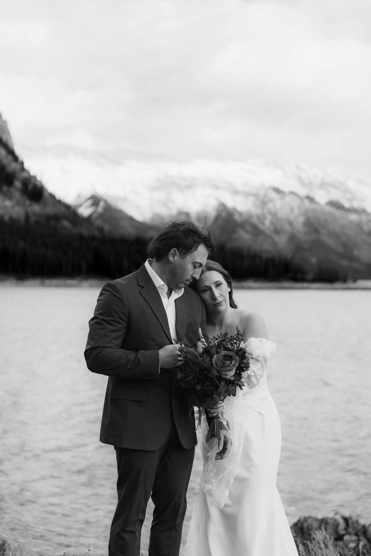 Black and white wedding photo of a couple sharing an intimate moment by a mountain lake.