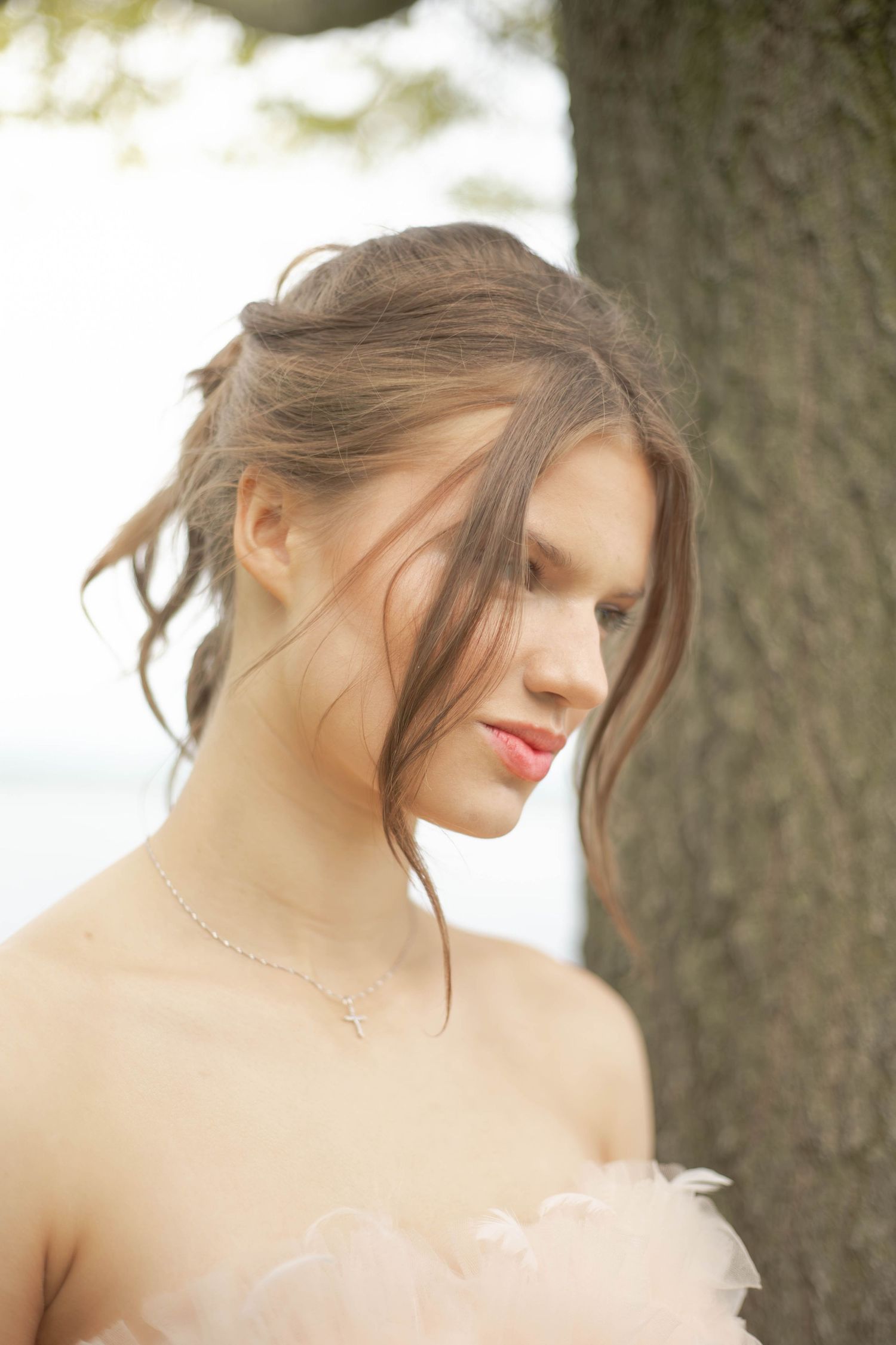 A dreamy bridal portrait shows a soft updo hairstyle and delicate lace gown against a blurred natural backdrop.