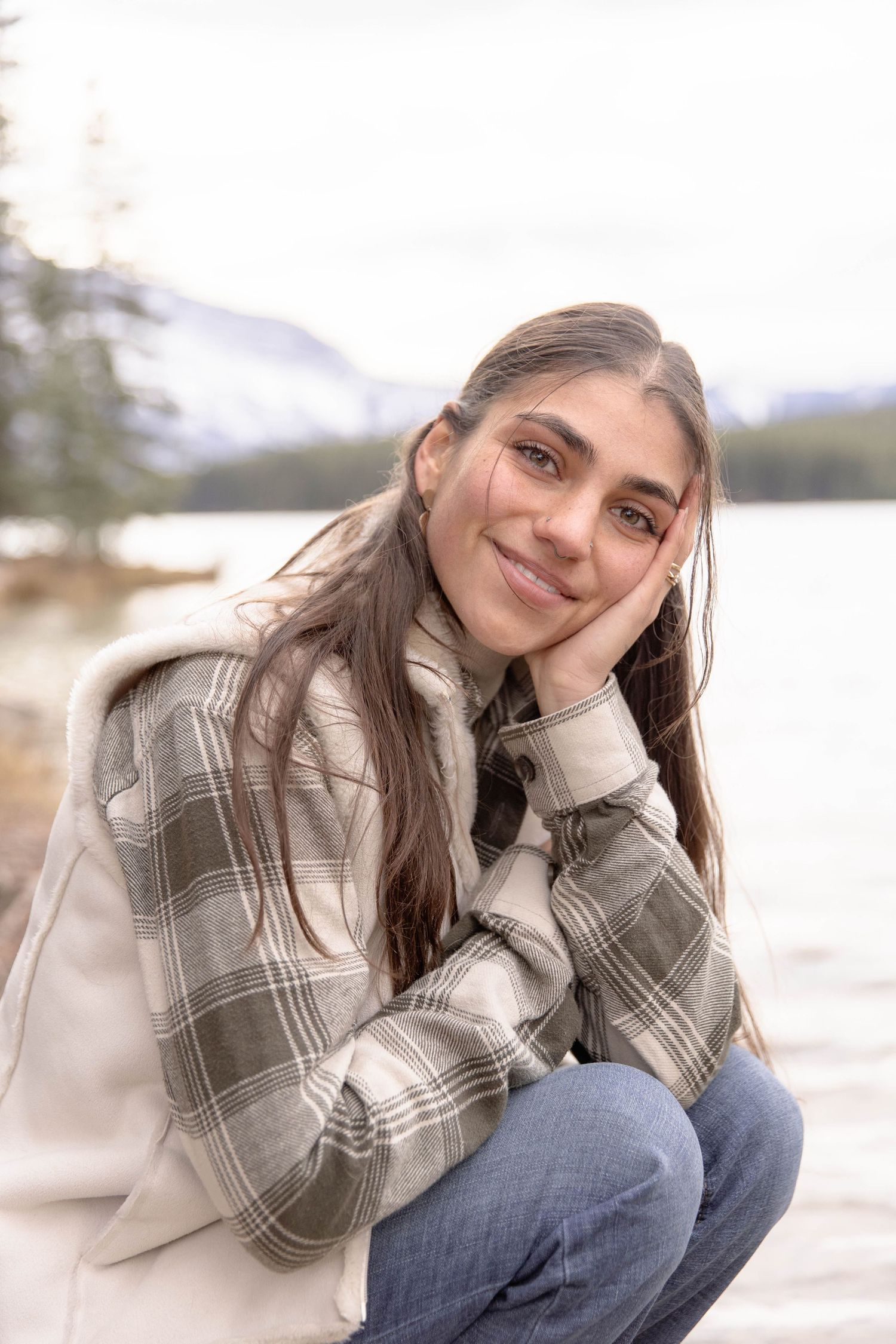 A person in a plaid jacket sits outdoors by a lake on a cloudy day, creating a cozy autumn atmosphere.
