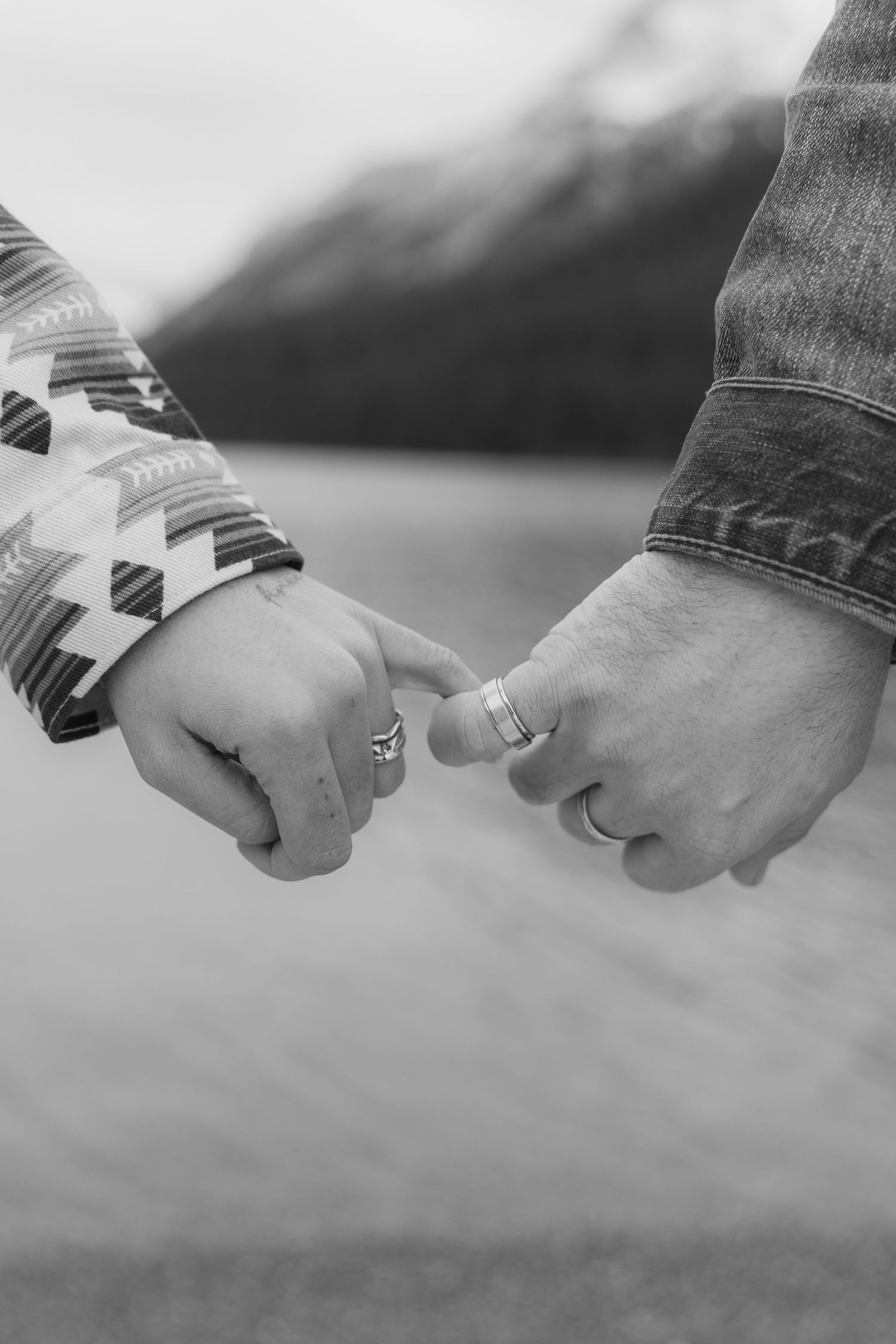 Black and white image of two hands holding each other in a loving gesture against a blurred background.