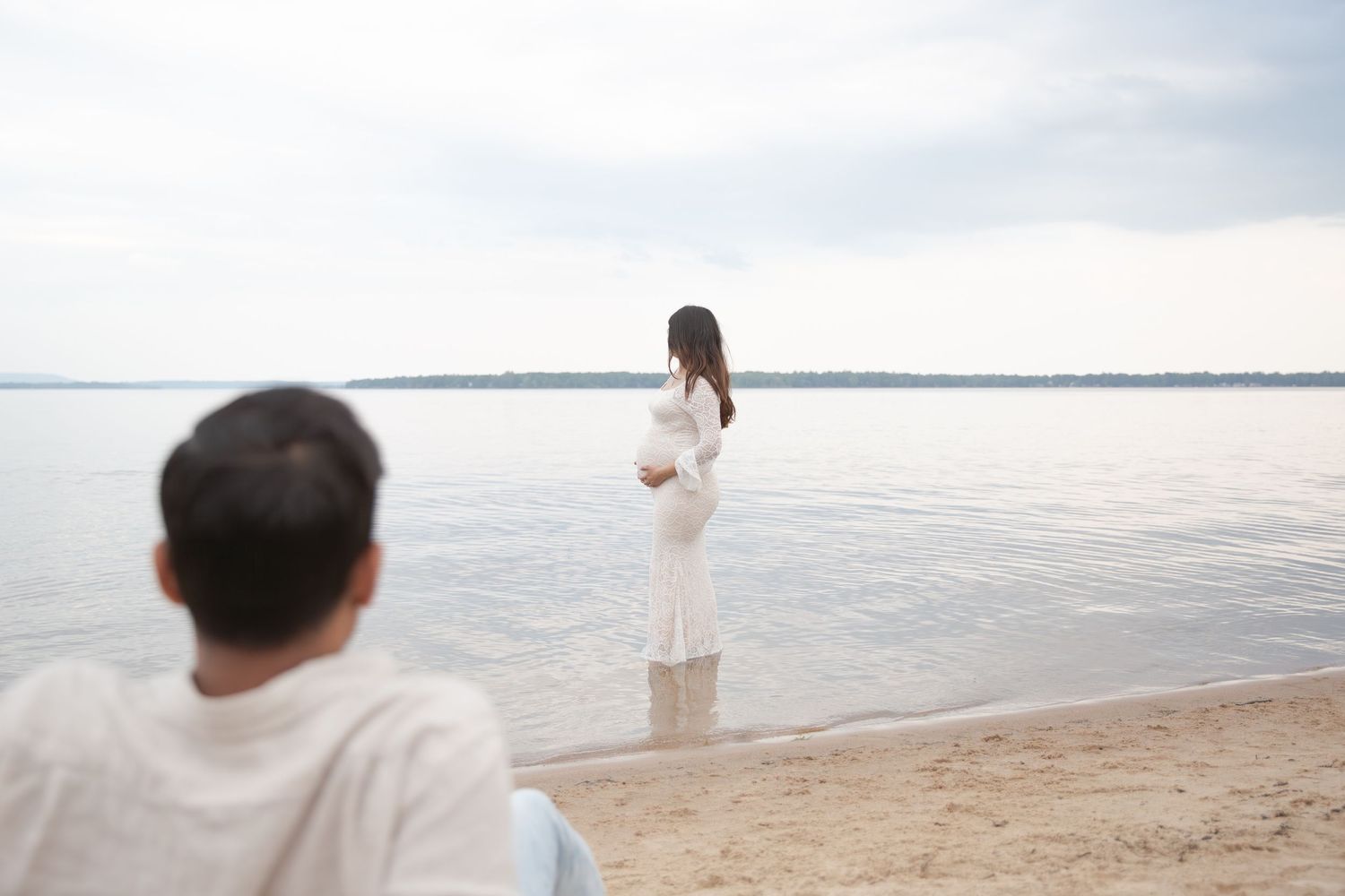A couple stands together on a sandy beach at sunset, creating a romantic silhouette against the ocean backdrop.
