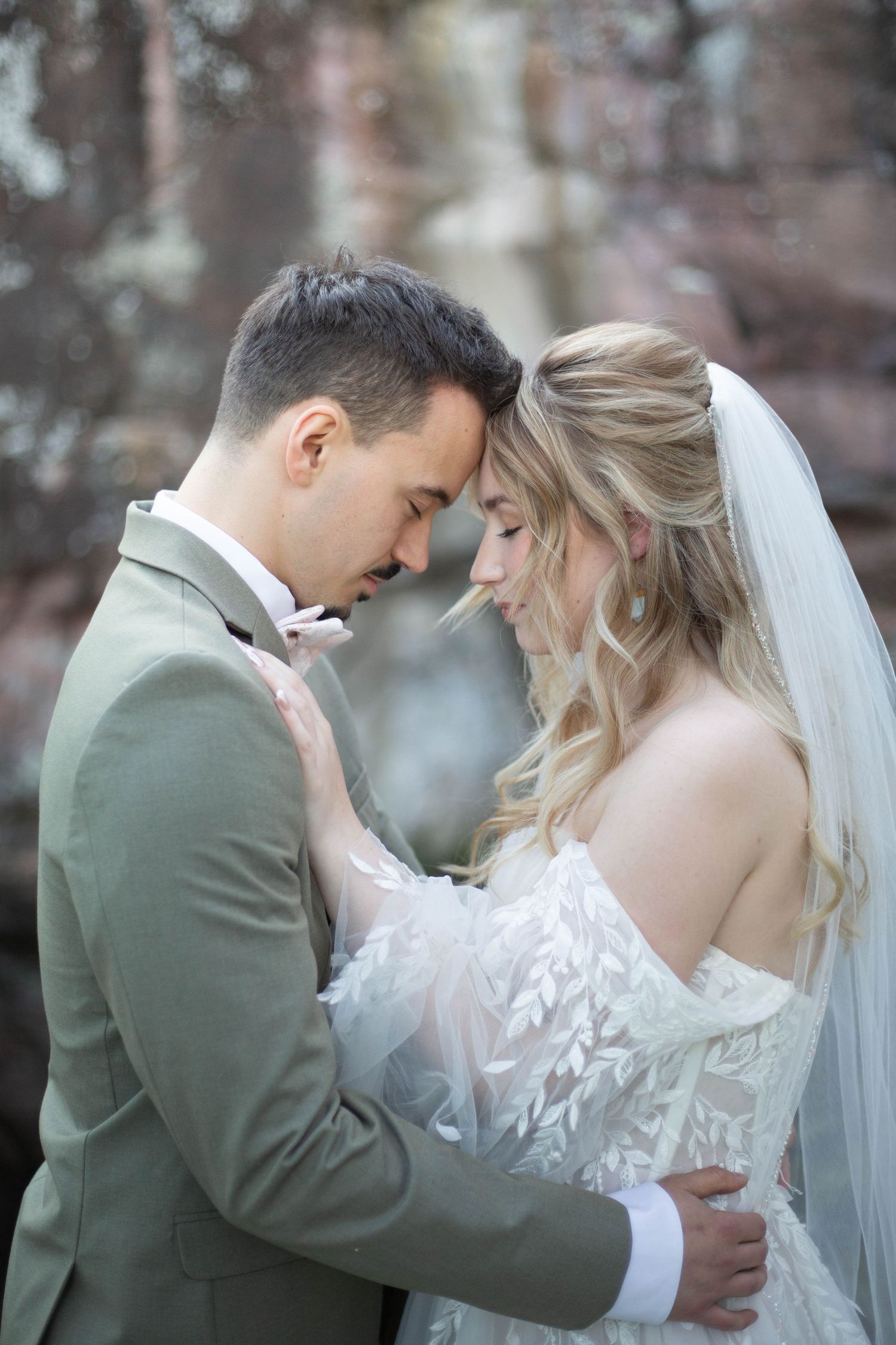 A romantic wedding portrait shows a couple sharing an intimate moment outdoors while wearing sage green and white attire.