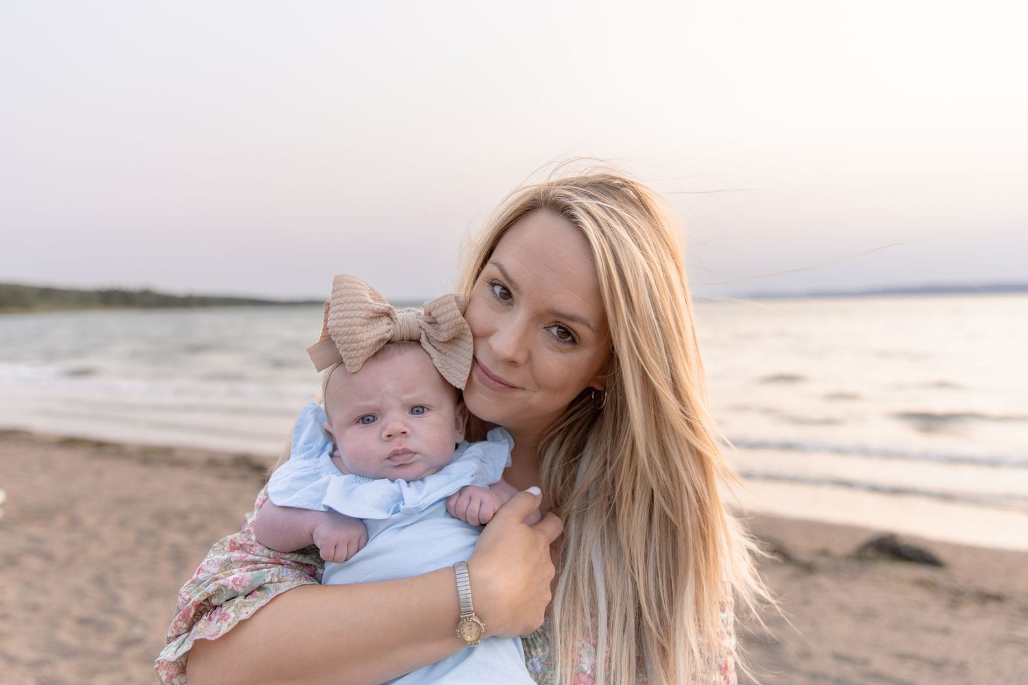 Tender seaside family moment captured at golden hour with gentle waves and sunset in the background.