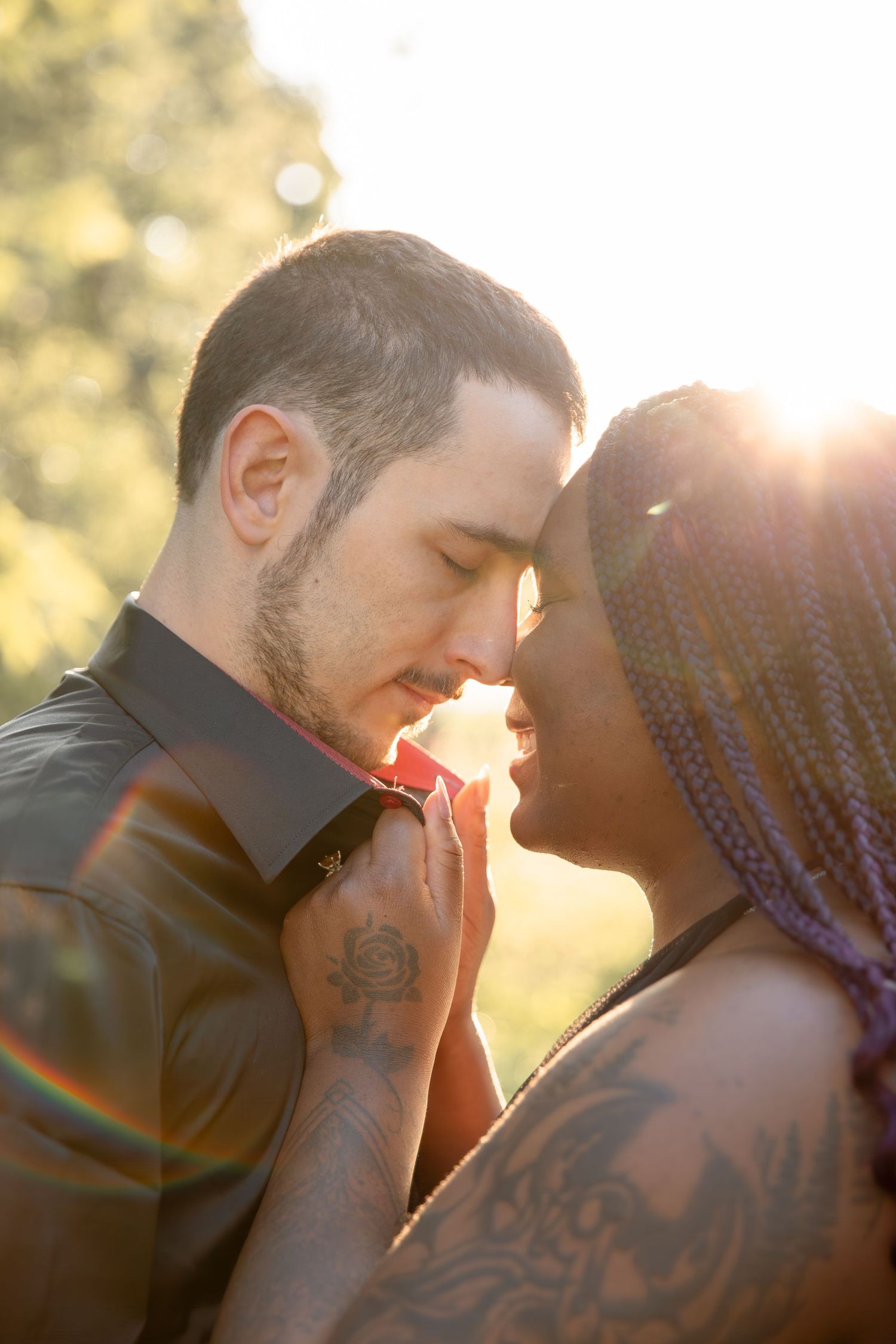 Intimate couple sharing tender moment at sunset's golden hour with lens flare and visible tattoos.