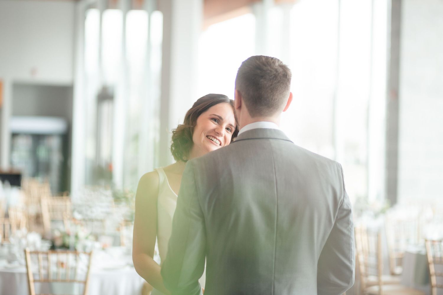 A bride and groom share a tender moment in an elegant wedding reception venue filled with soft natural light.