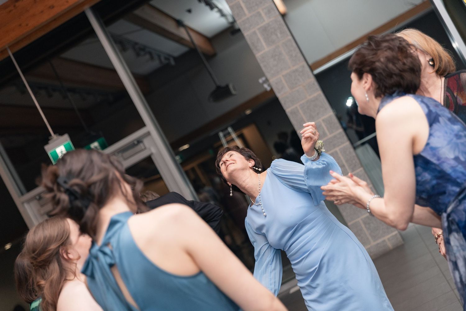 Women in blue dresses dancing joyfully outdoors at a social event near a modern building.