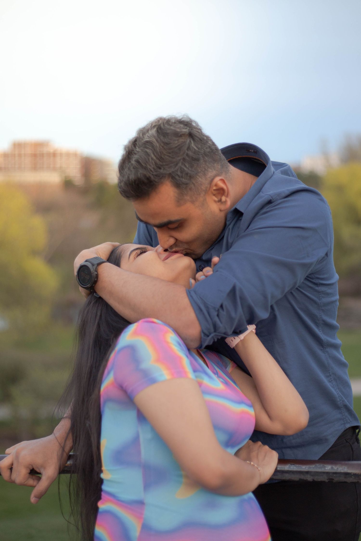 A romantic couple shares an intimate moment while embracing outdoors against a blurred natural background.