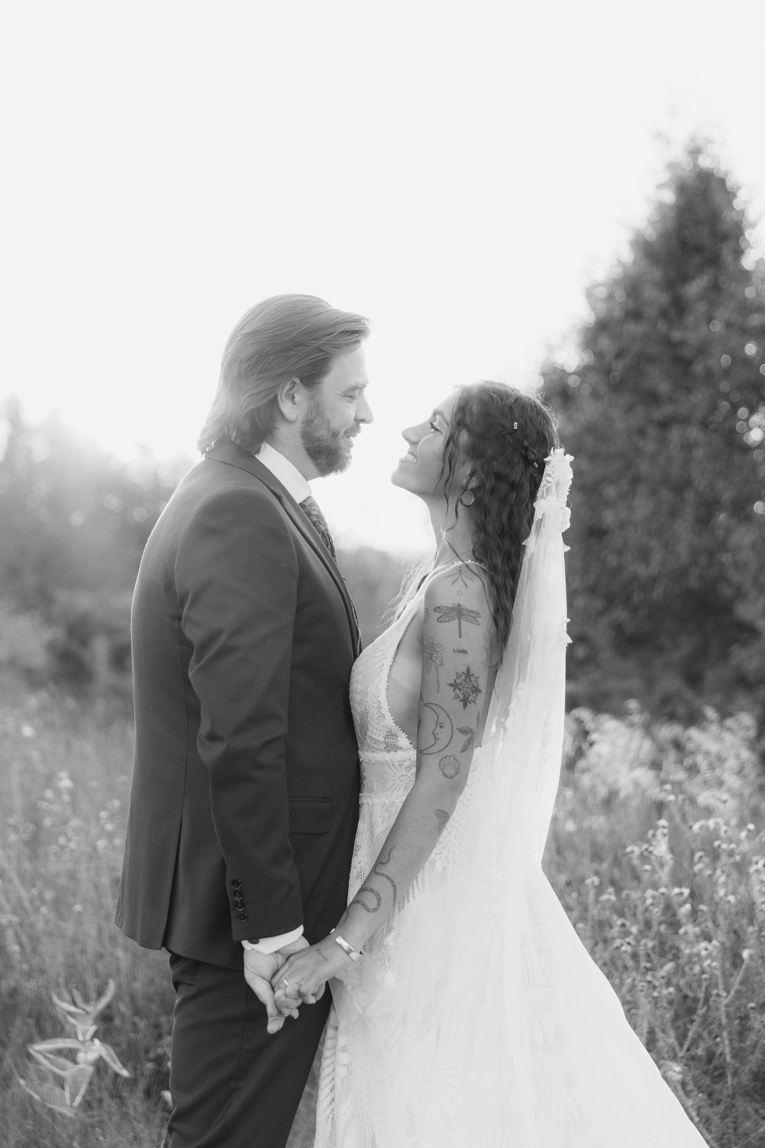 Black and white wedding photos show a romantic couple embracing in a wildflower meadow at sunset.