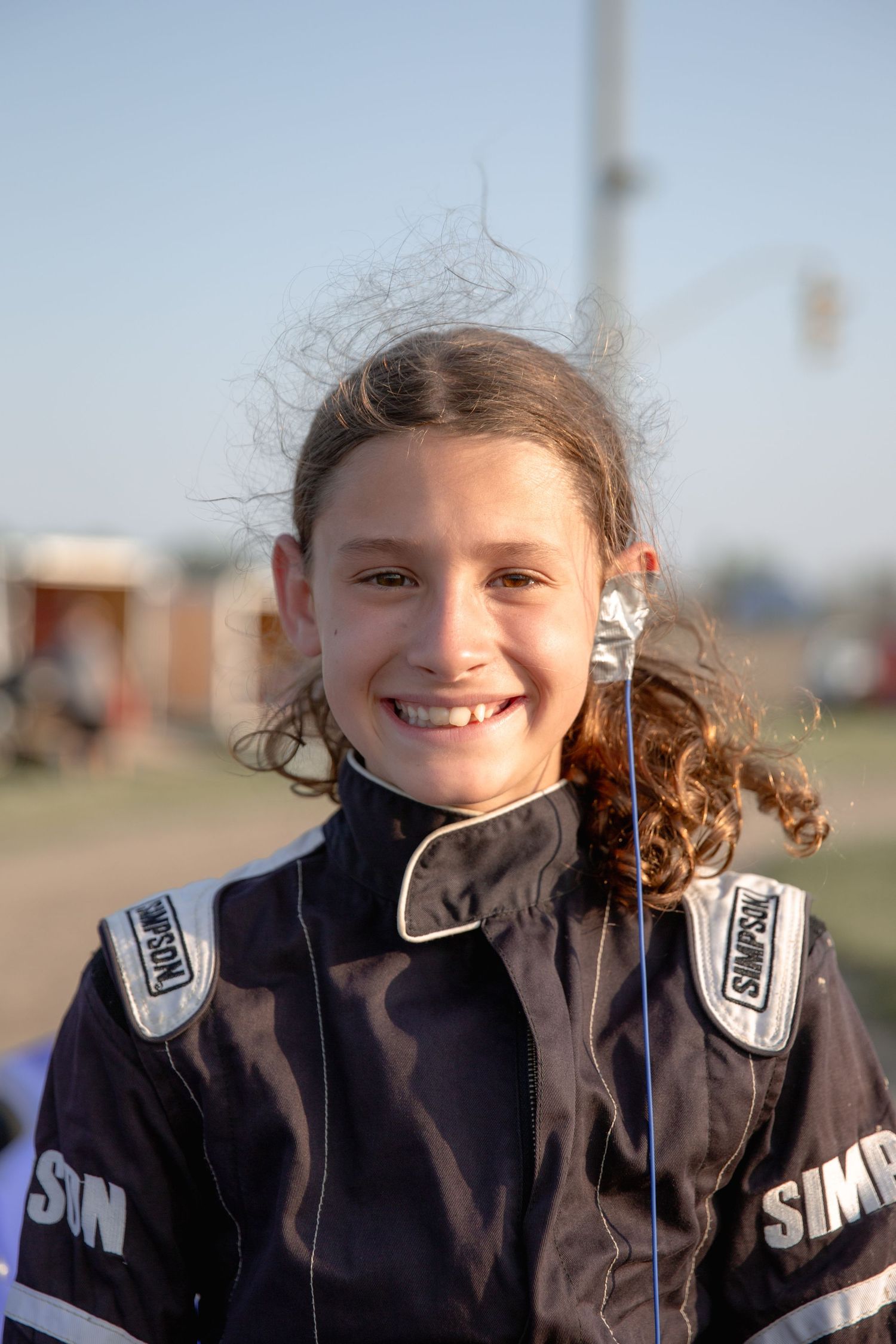 A series of cheerful portrait shots showing a young person in a black SimplyPlan jacket with curly hair blowing in the wind.