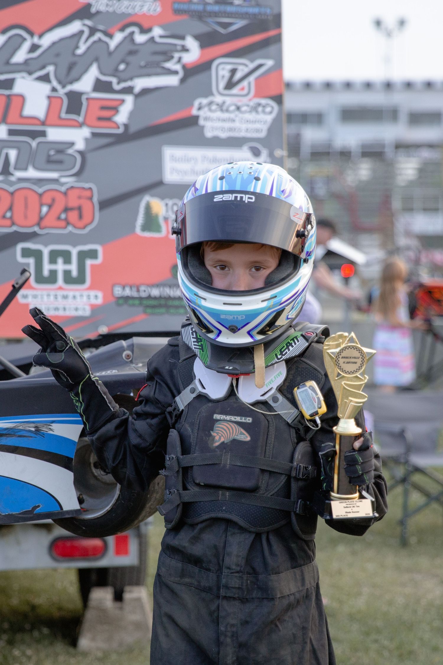 A series of similar shots showing a motorsport driver holding up race trophies while wearing a black racing suit and helmet.