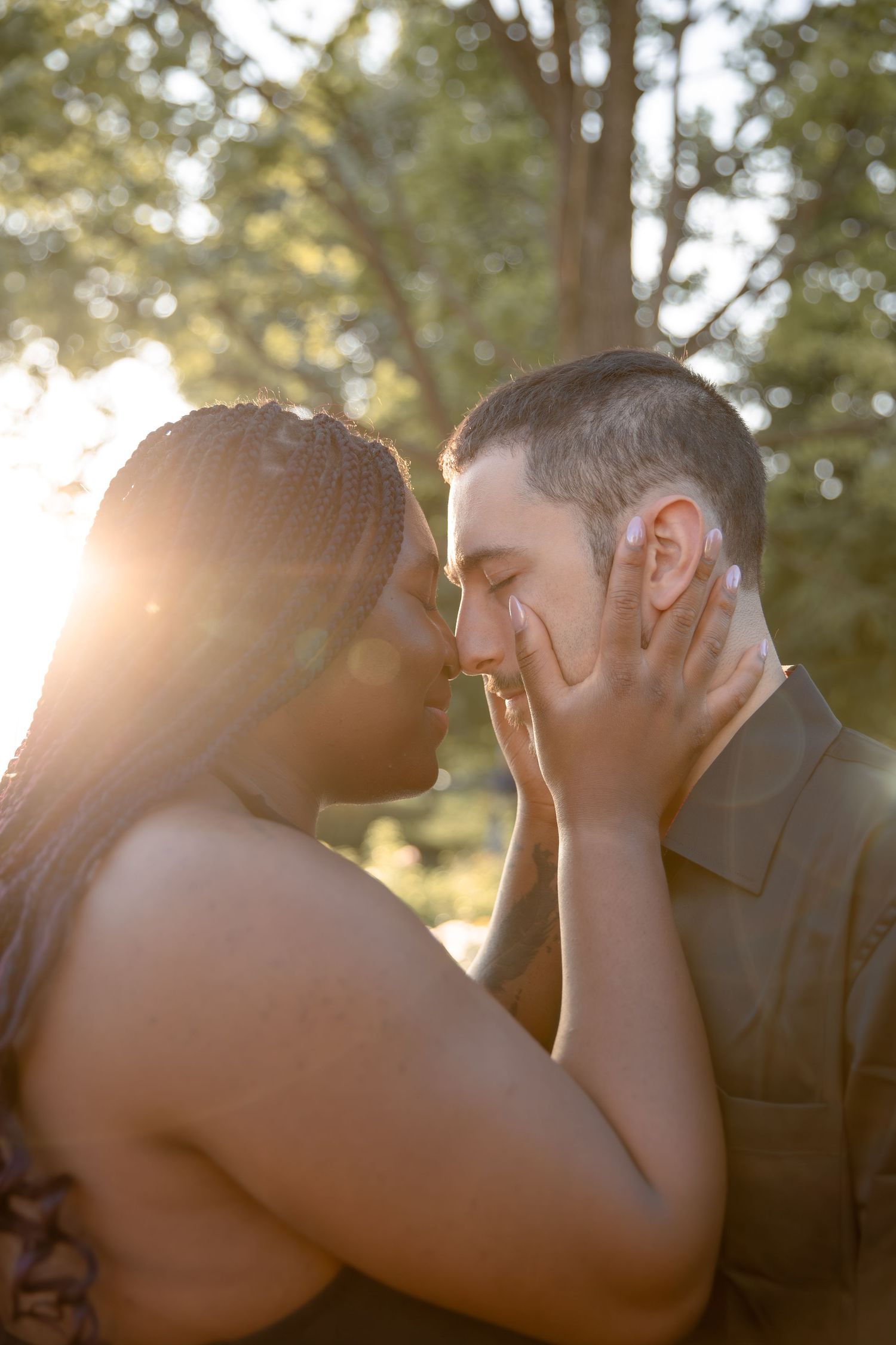 A romantic moment between a couple embracing in golden sunlight with trees in the background.