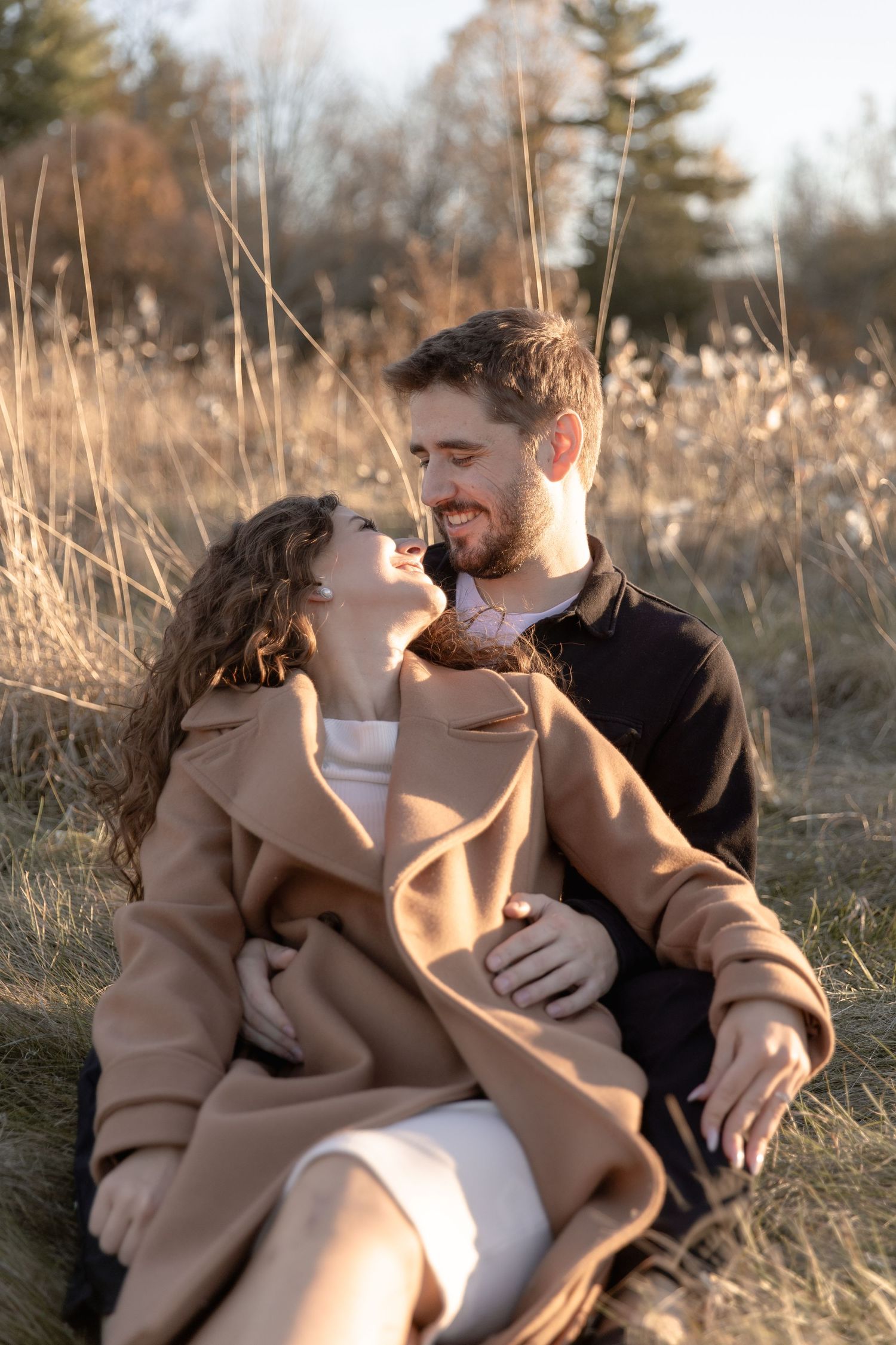 A couple sits together in tall grass during golden hour sharing intimate moments in a series of romantic photos.
