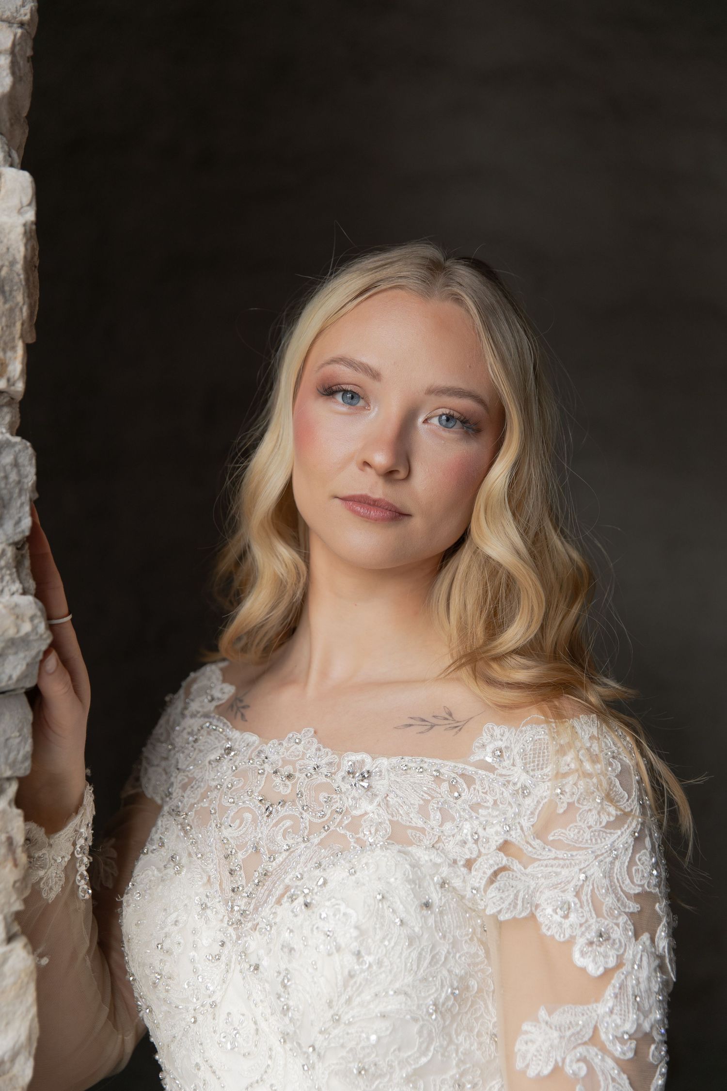 A bride in a white lace wedding dress with long sleeves poses against a dark background in a photo series.