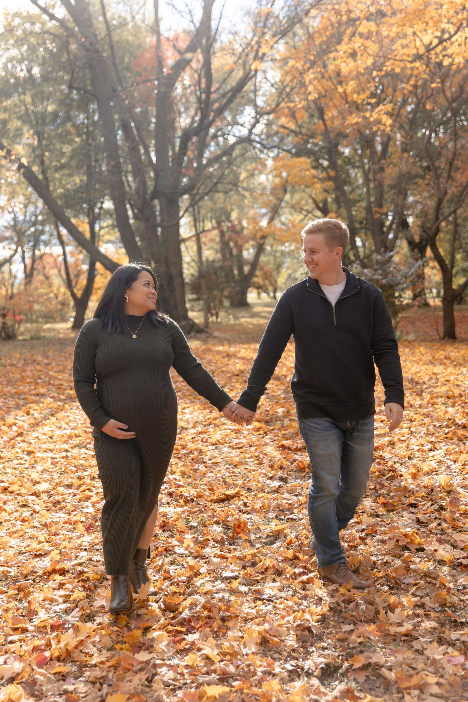 Two people walk together through a park filled with golden autumn leaves scattered across the ground.
