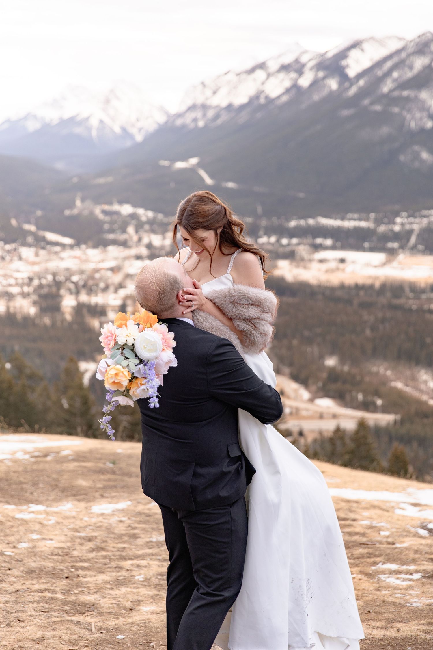 A couple shares an intimate moment during their winter mountain wedding in Banff with snow-capped peaks in the background.
