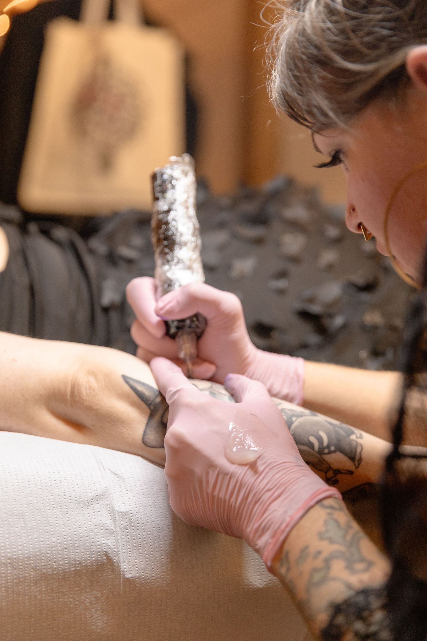 A tattoo artist wearing pink gloves carefully works on a client's skin during a detailed tattoo session.