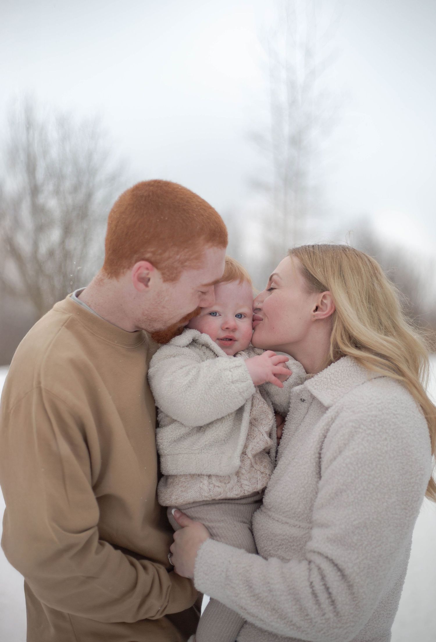A family shares an intimate moment of affection in winter while wearing neutral colored clothing.