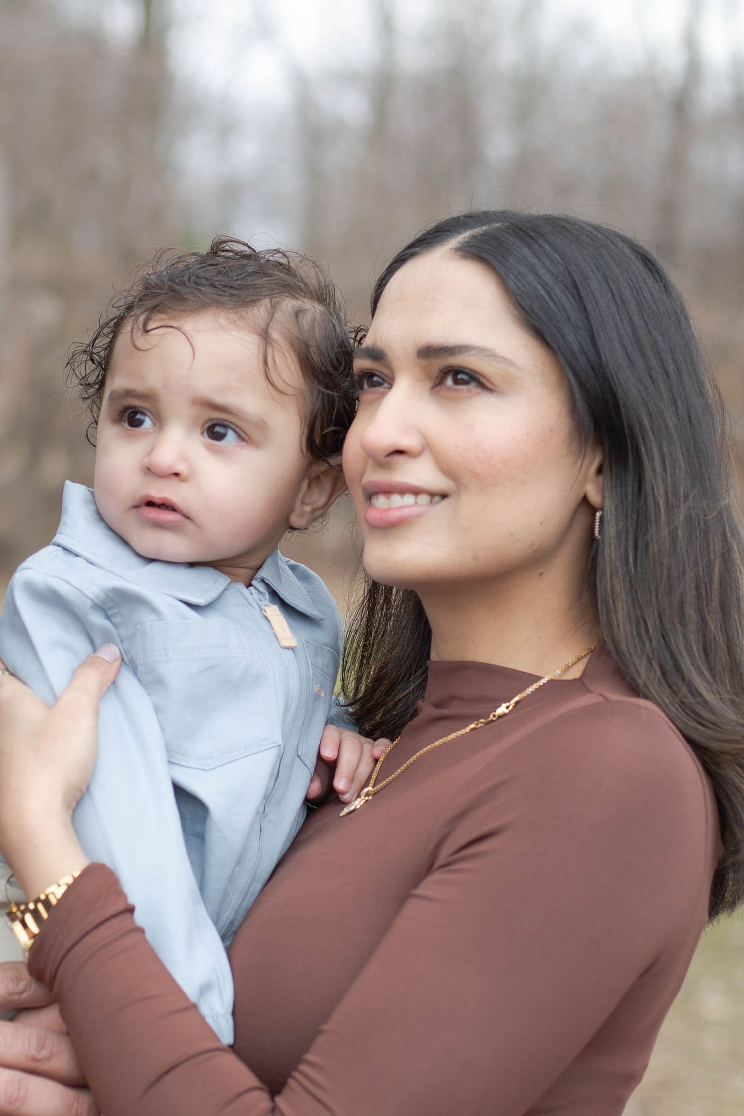 A parent and toddler share a tender moment outdoors on an autumn day, both wearing coordinated earth-toned outfits.