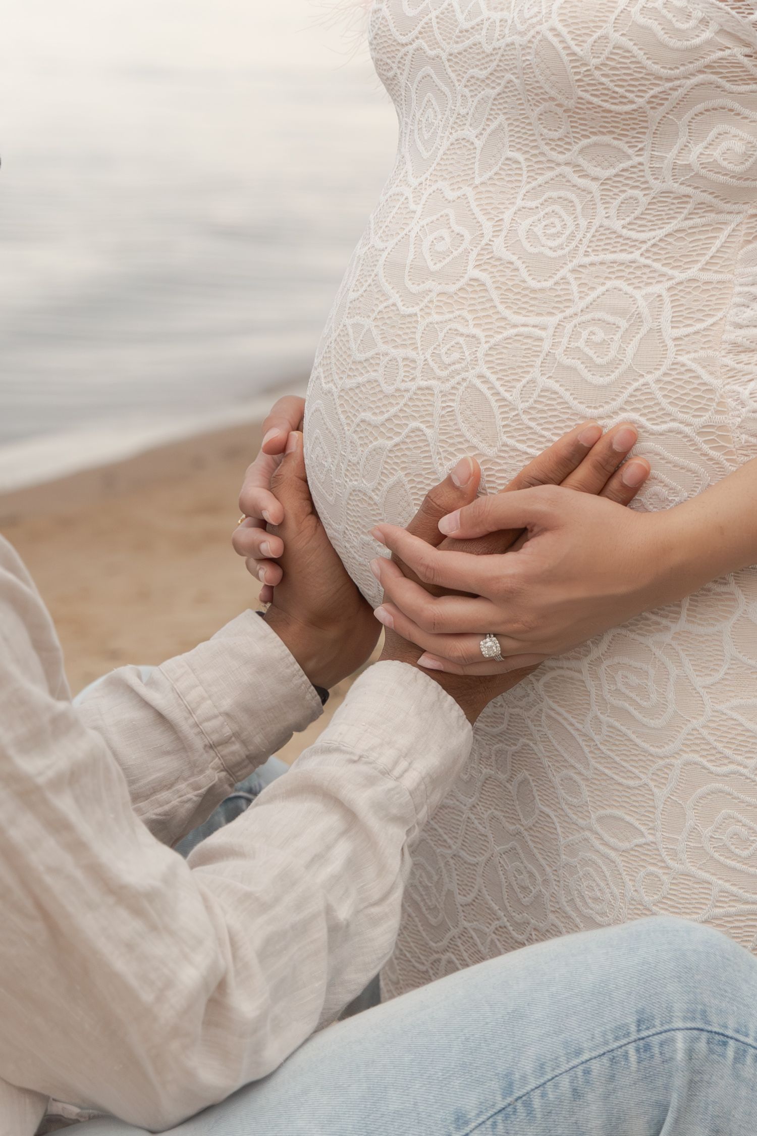 Delicate hands hold intricate white lace fabric against a soft, light-colored background, showing fine embroidered details.