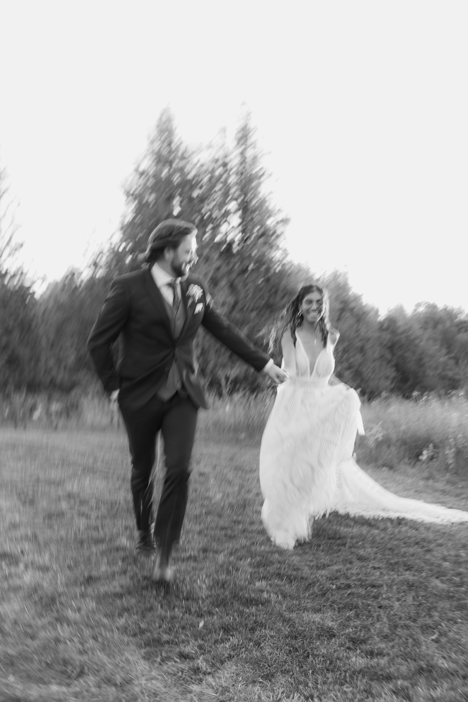 A playful black and white photo series shows a couple running through a field in wedding attire.