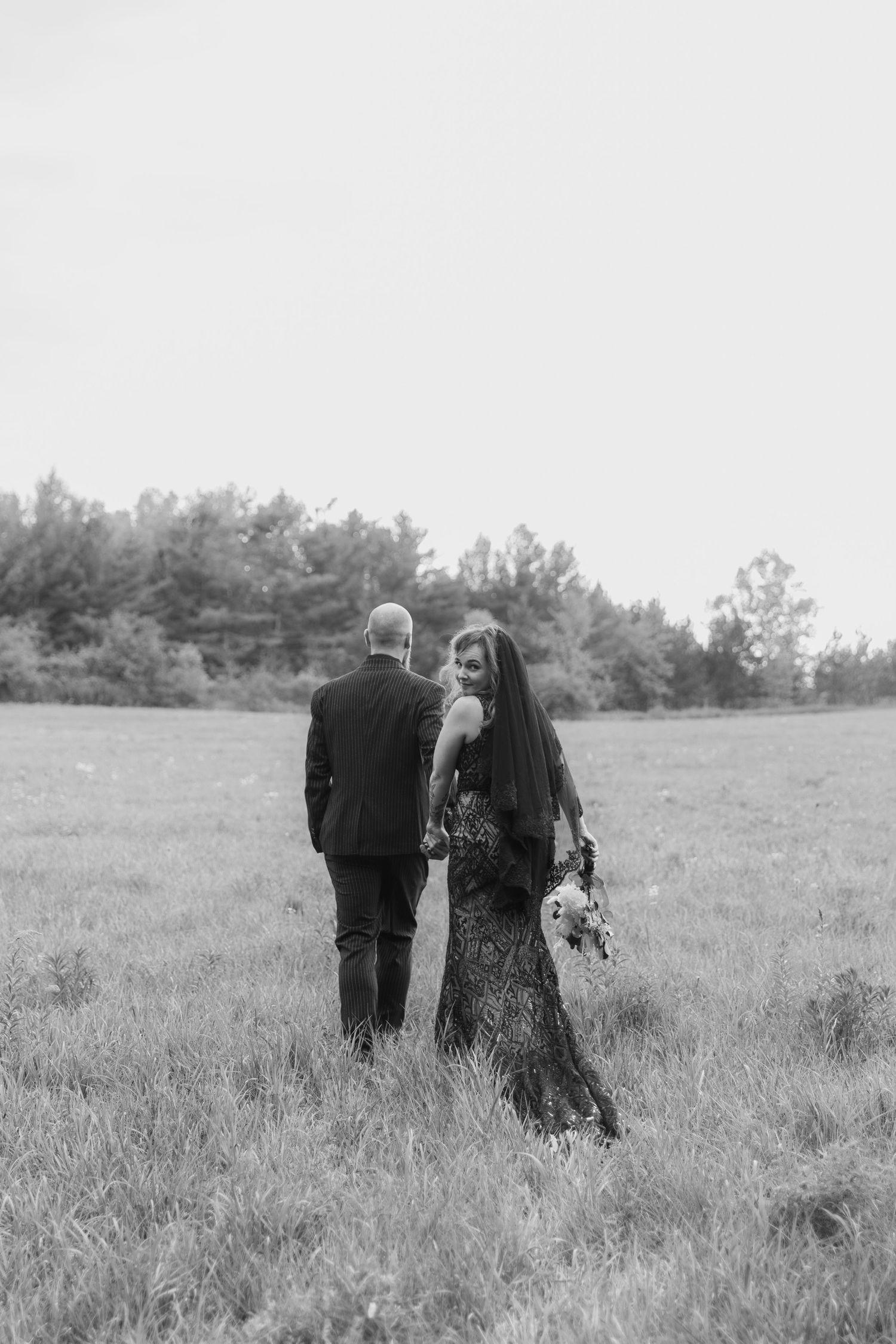 A couple in dark clothing walks together through a serene meadow in black and white photography.