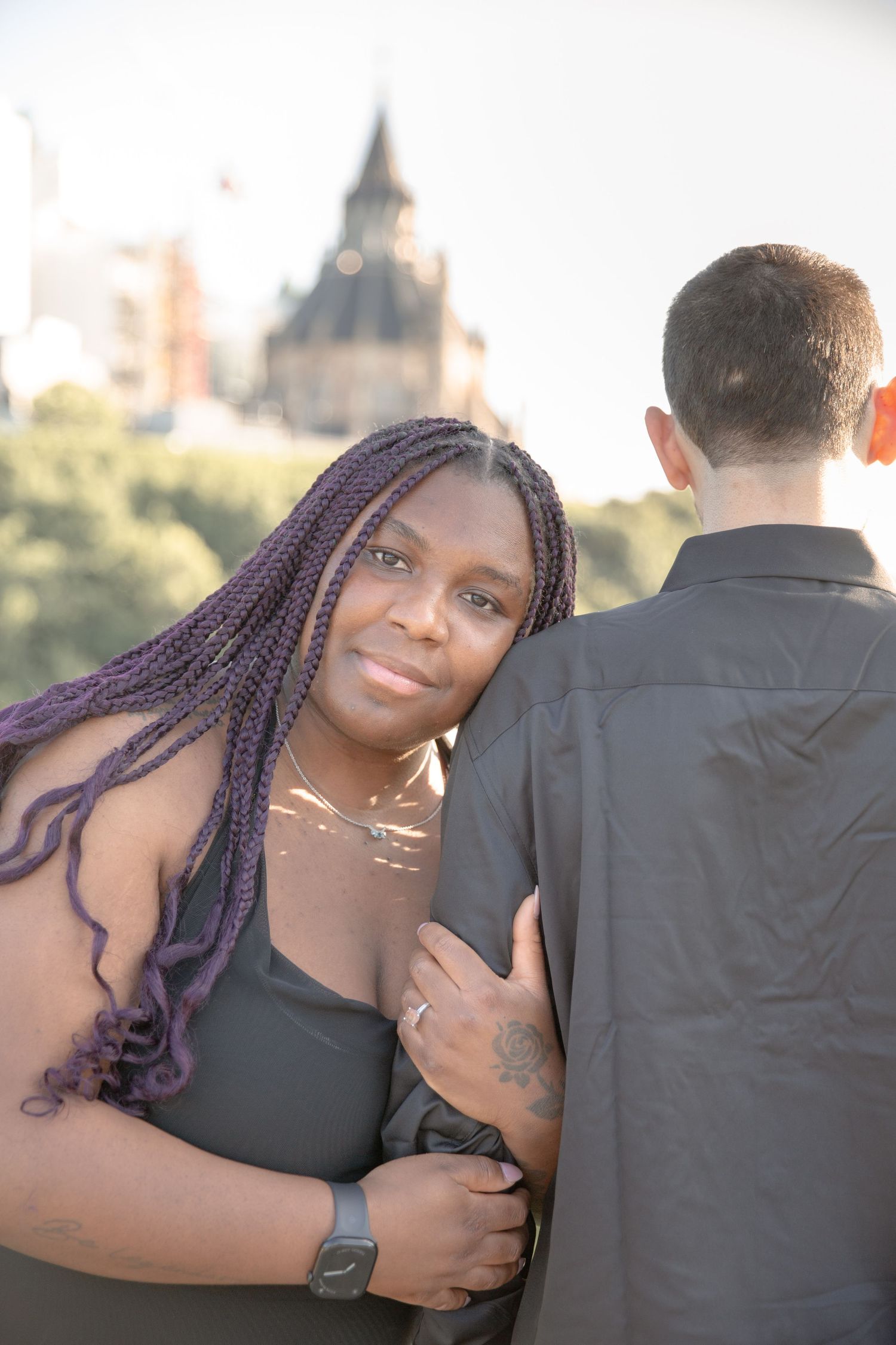Couple poses together outdoors with a church spire visible in the background during golden hour.