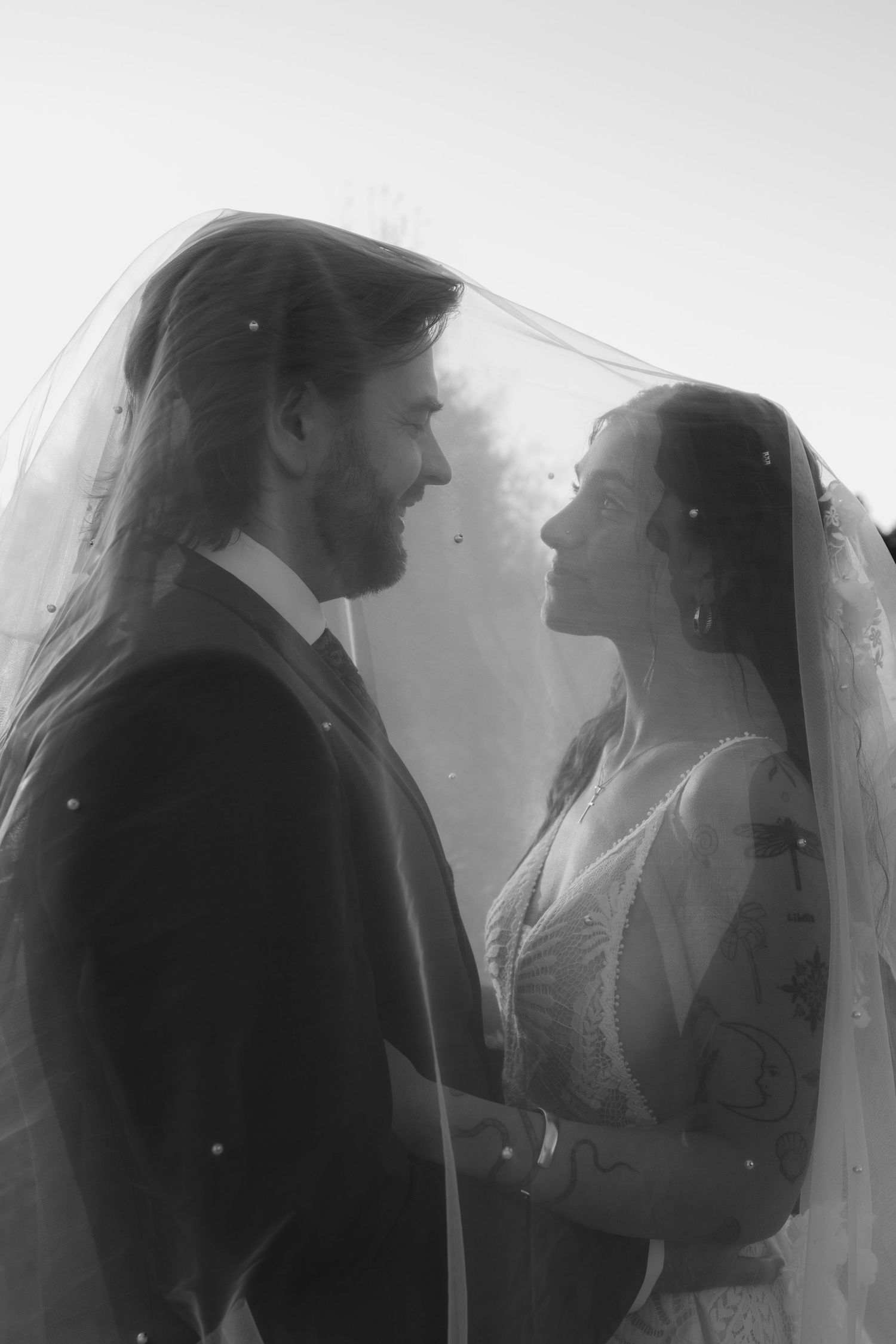 A romantic black and white wedding portrait of a couple in formal attire gazing at each other through the bride's veil.