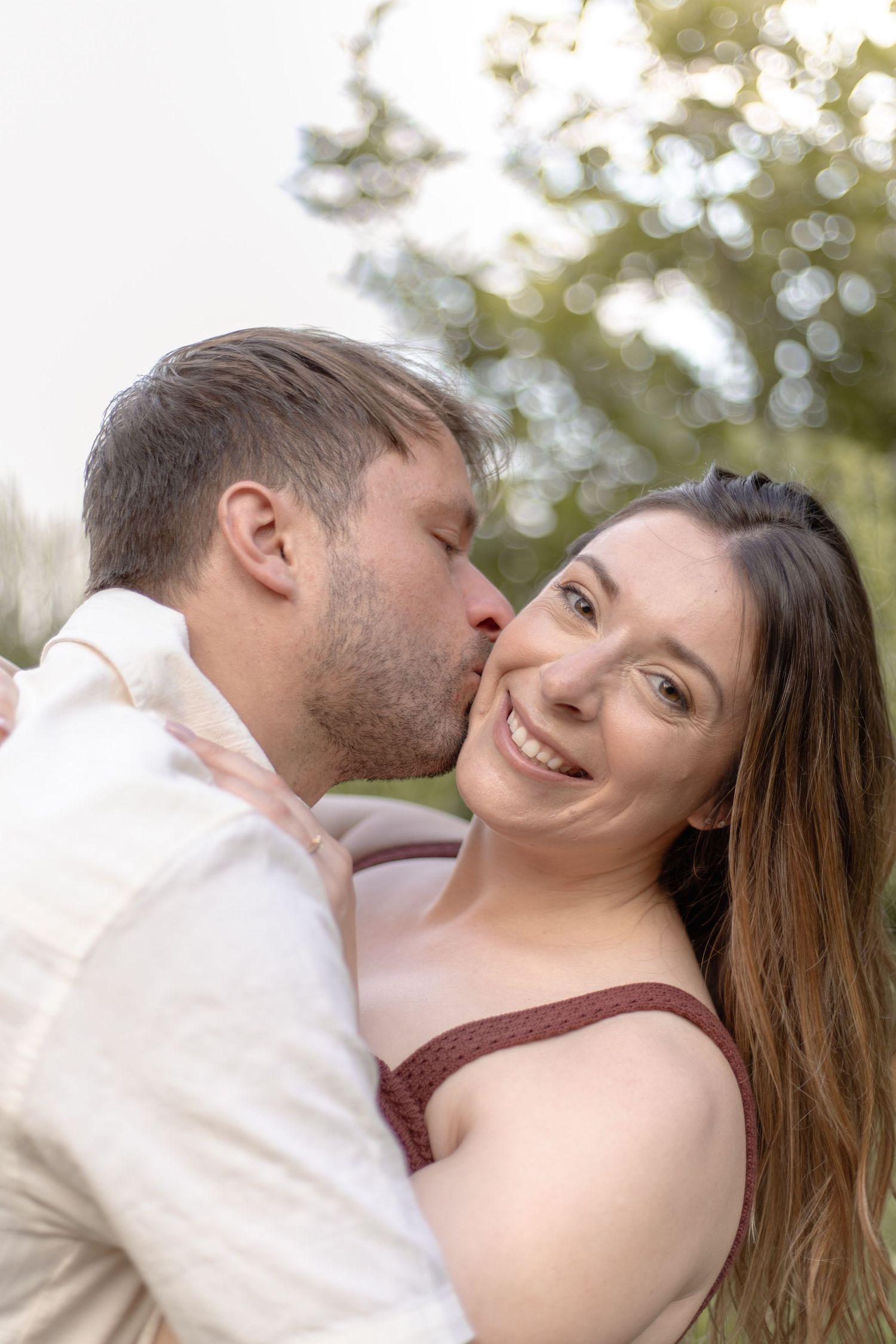 A romantic couple shares tender moments together outdoors with soft bokeh lighting in the background.