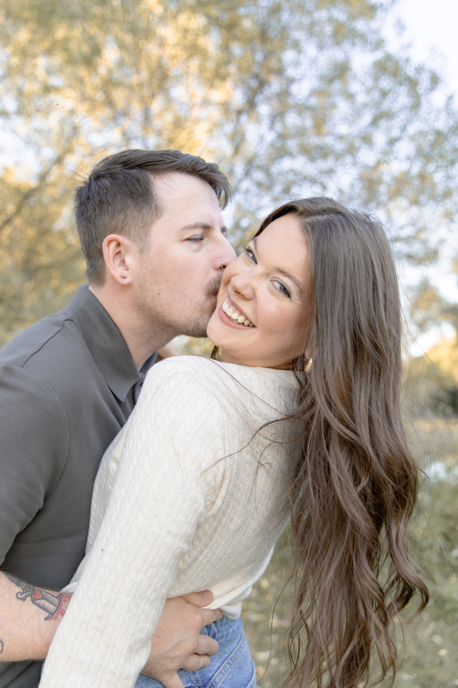 A couple shares a tender moment outdoors in autumn, with the person in grey embracing their partner in a cream sweater.