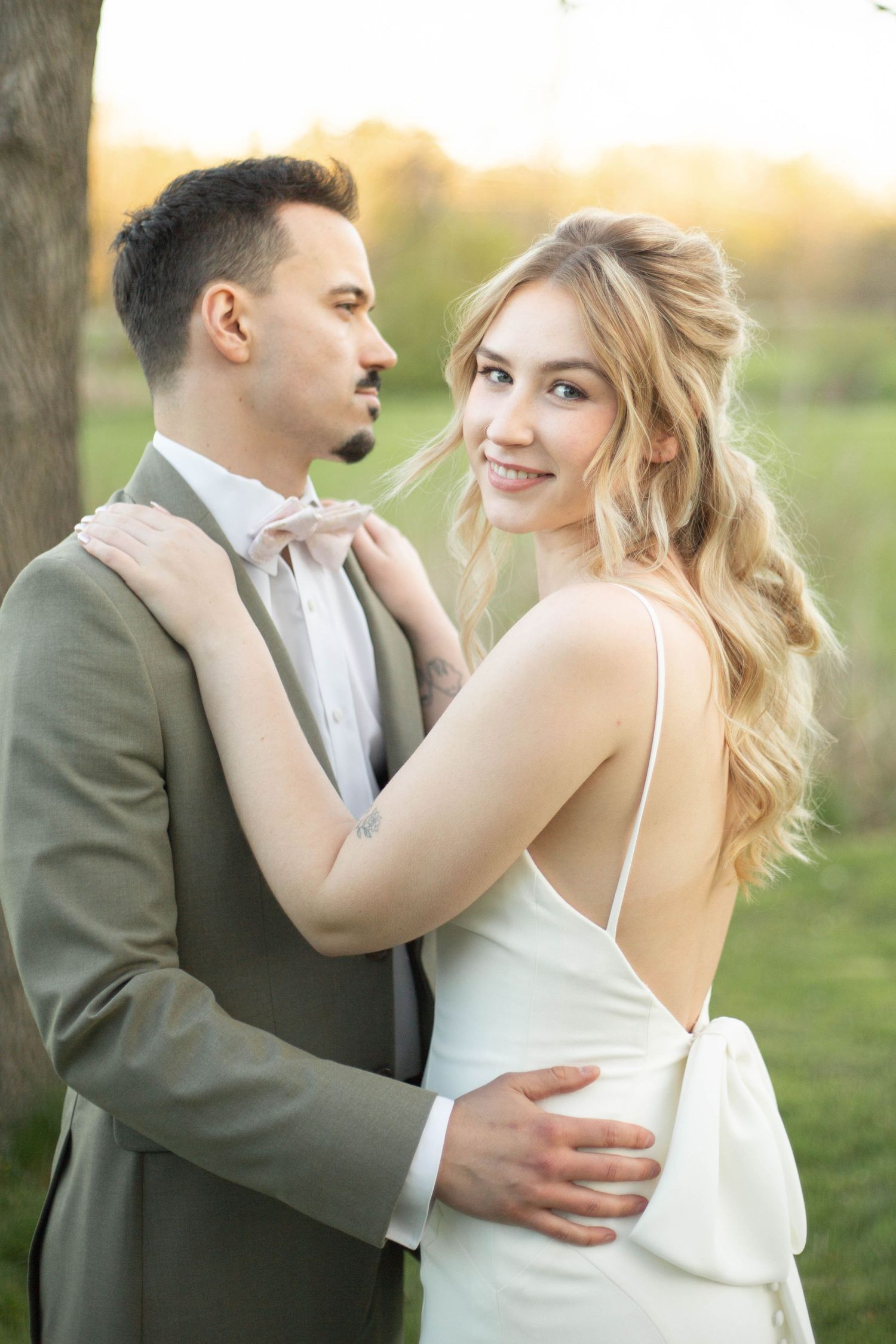 A romantic outdoor wedding portrait of a couple at sunset, with the bride in white and groom in gray suit.