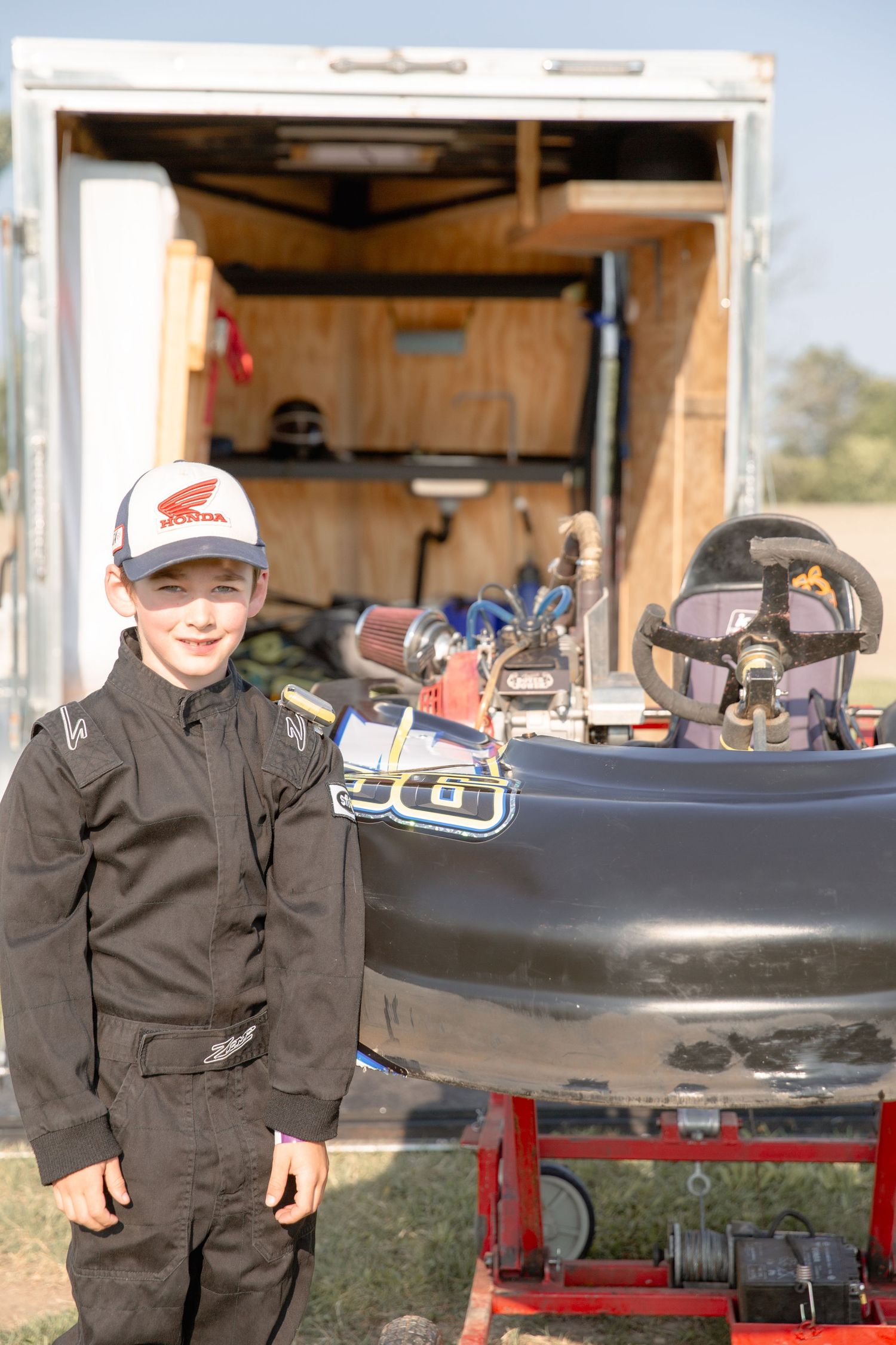 Child-sized karting equipment and gear sits on outdoor racks at a racing facility on a sunny day.