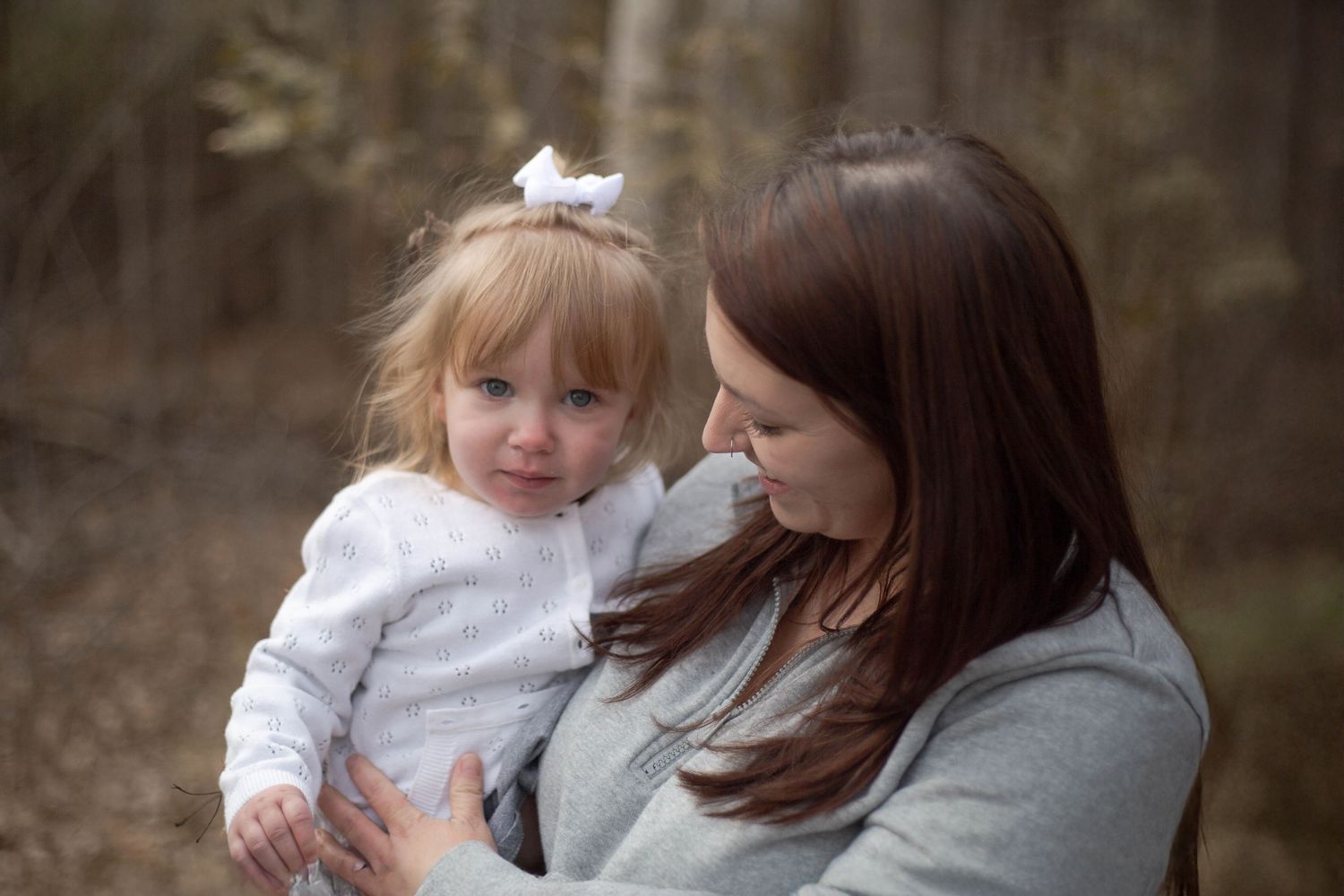 An intimate outdoor portrait of a mom and toddler wearing white sharing a close moment together.