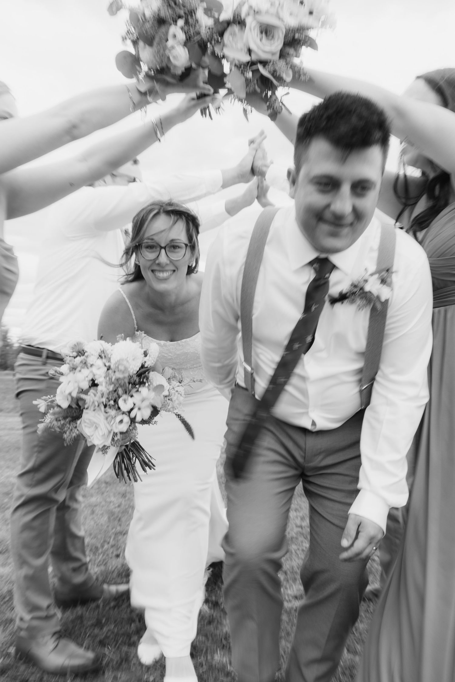 Black and white wedding photo showing a joyful couple walking together outdoors with the bride holding a floral bouquet.