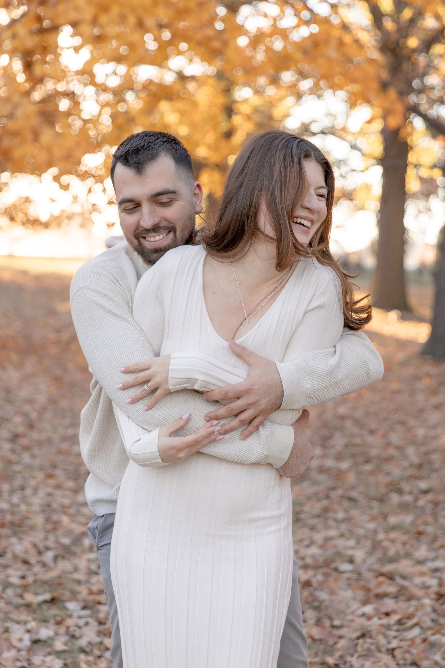 Joyful couple sharing laughter during autumn photoshoot with golden leaves in background.