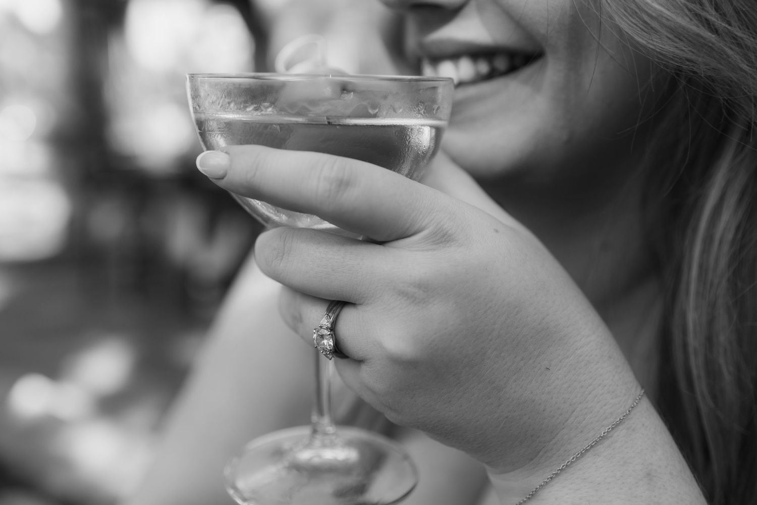 Close up black and white photo of hands holding an elegant cocktail glass with joyful expression.