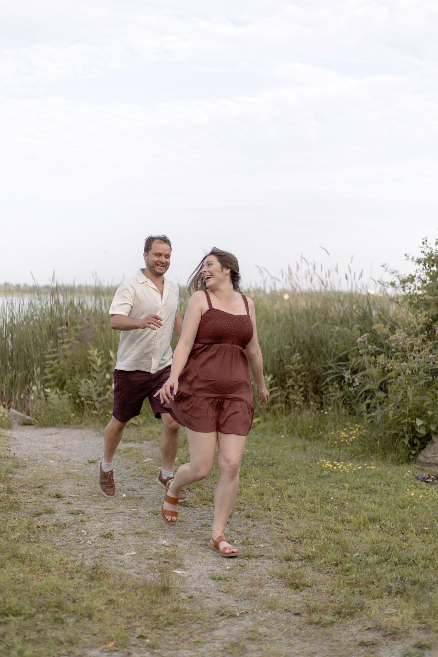 A couple playfully runs and skips together through a grassy field on a sunny day.
