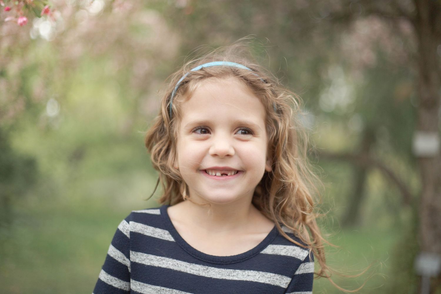 A child in a striped shirt smiles while playing outdoors on a sunny day in a natural setting.