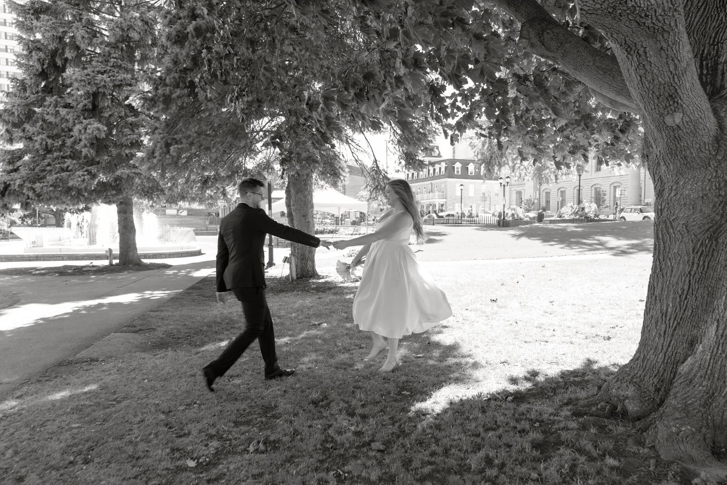 A romantic wedding couple dances together under large trees in a forest setting creating a dreamy atmosphere.