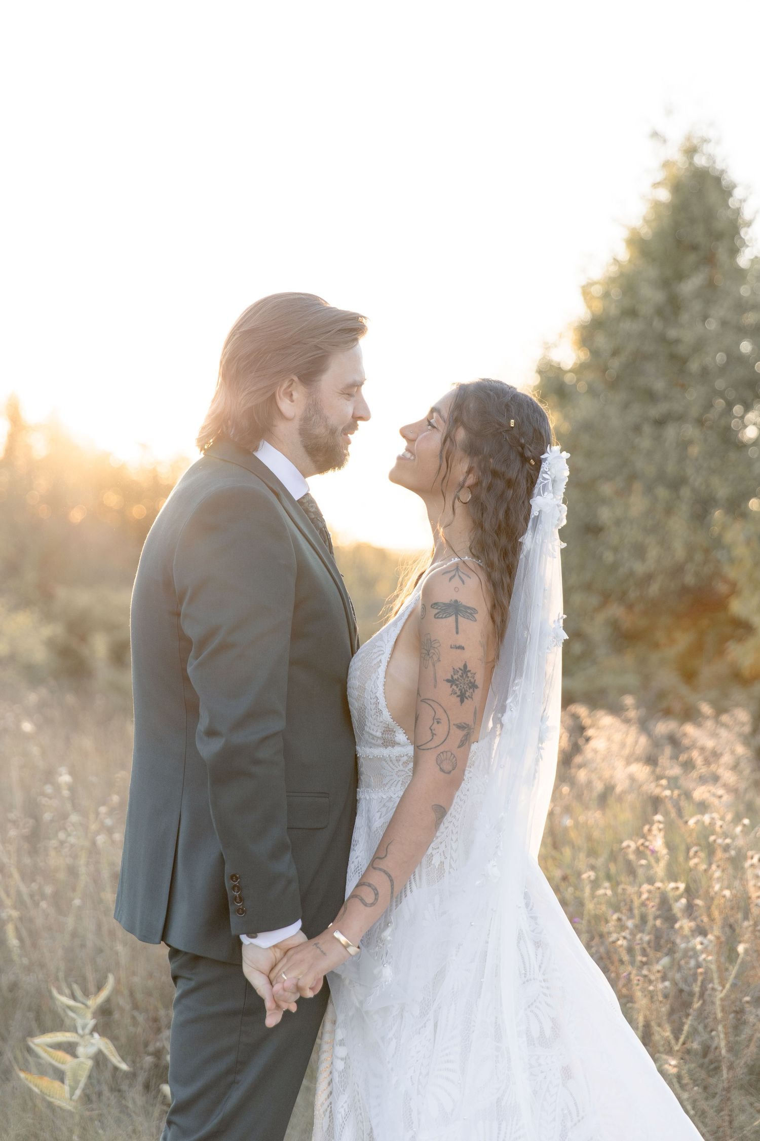 A couple in wedding attire shares intimate moments in a sunlit field during golden hour.