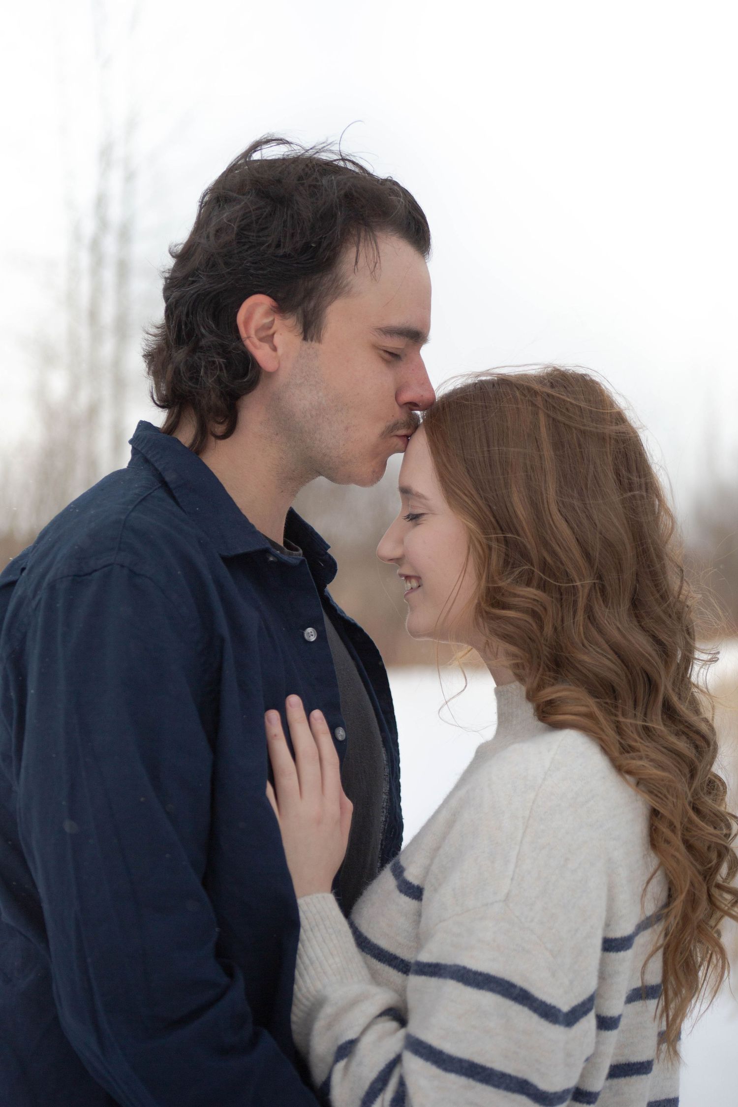 A romantic winter engagement photo showing a couple in an intimate embrace against a snowy backdrop.