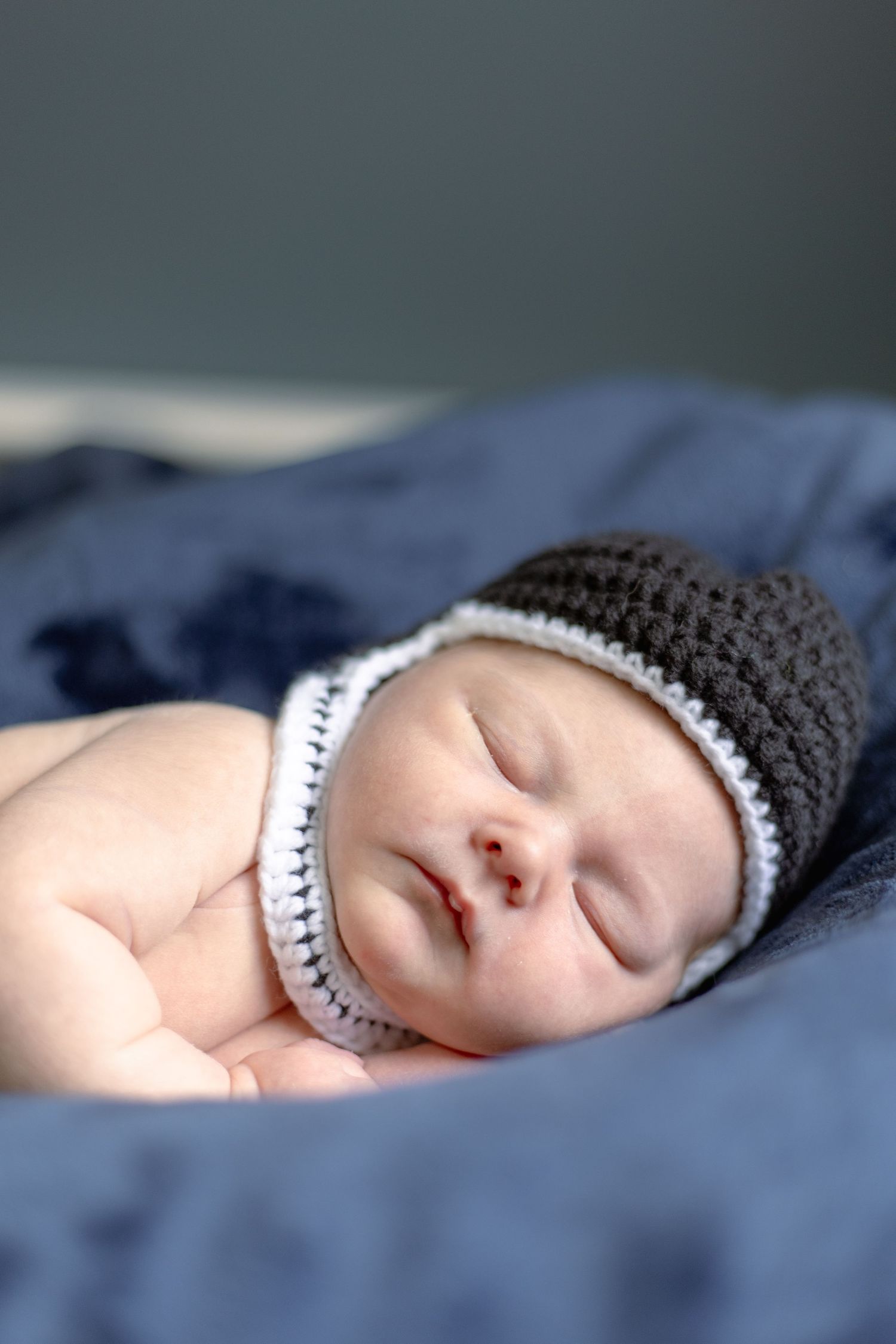 A sleeping baby wearing a gray and white knitted beanie hat rests peacefully on blue bedding.