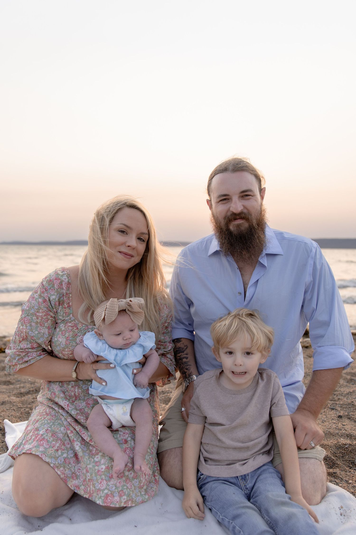 Family enjoying a sunset beach photoshoot while sitting on a blanket near the ocean.