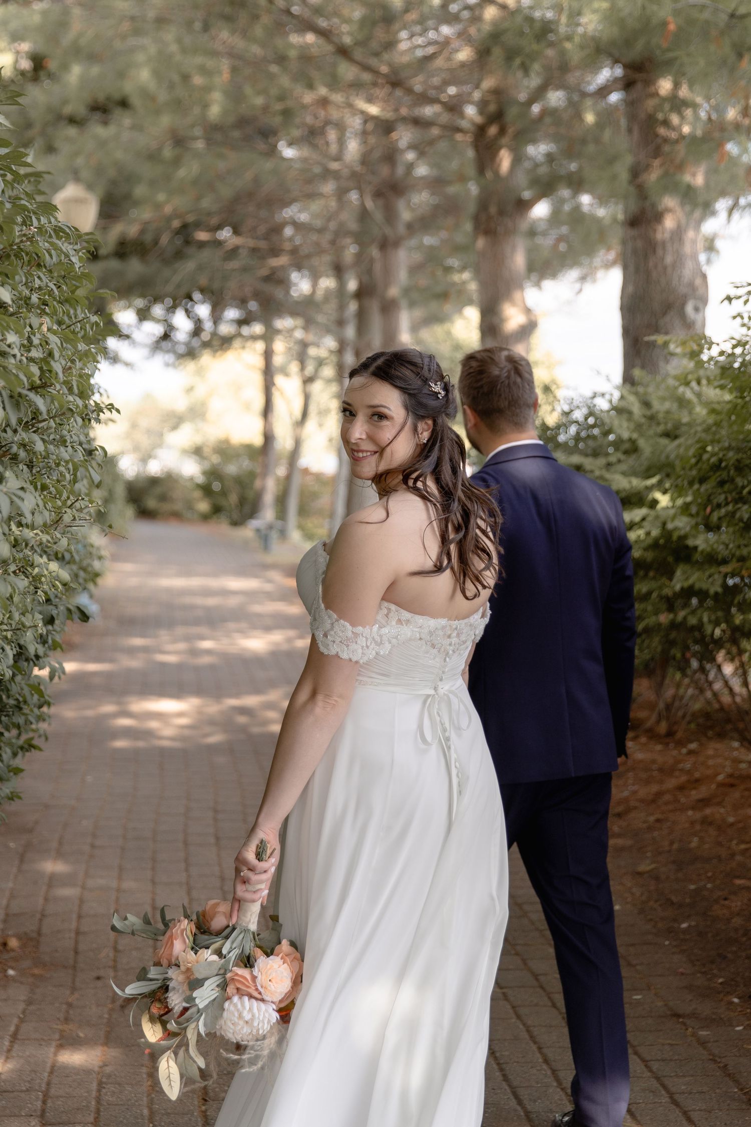 A couple in wedding attire walks along a tree-lined brick path on their special day.