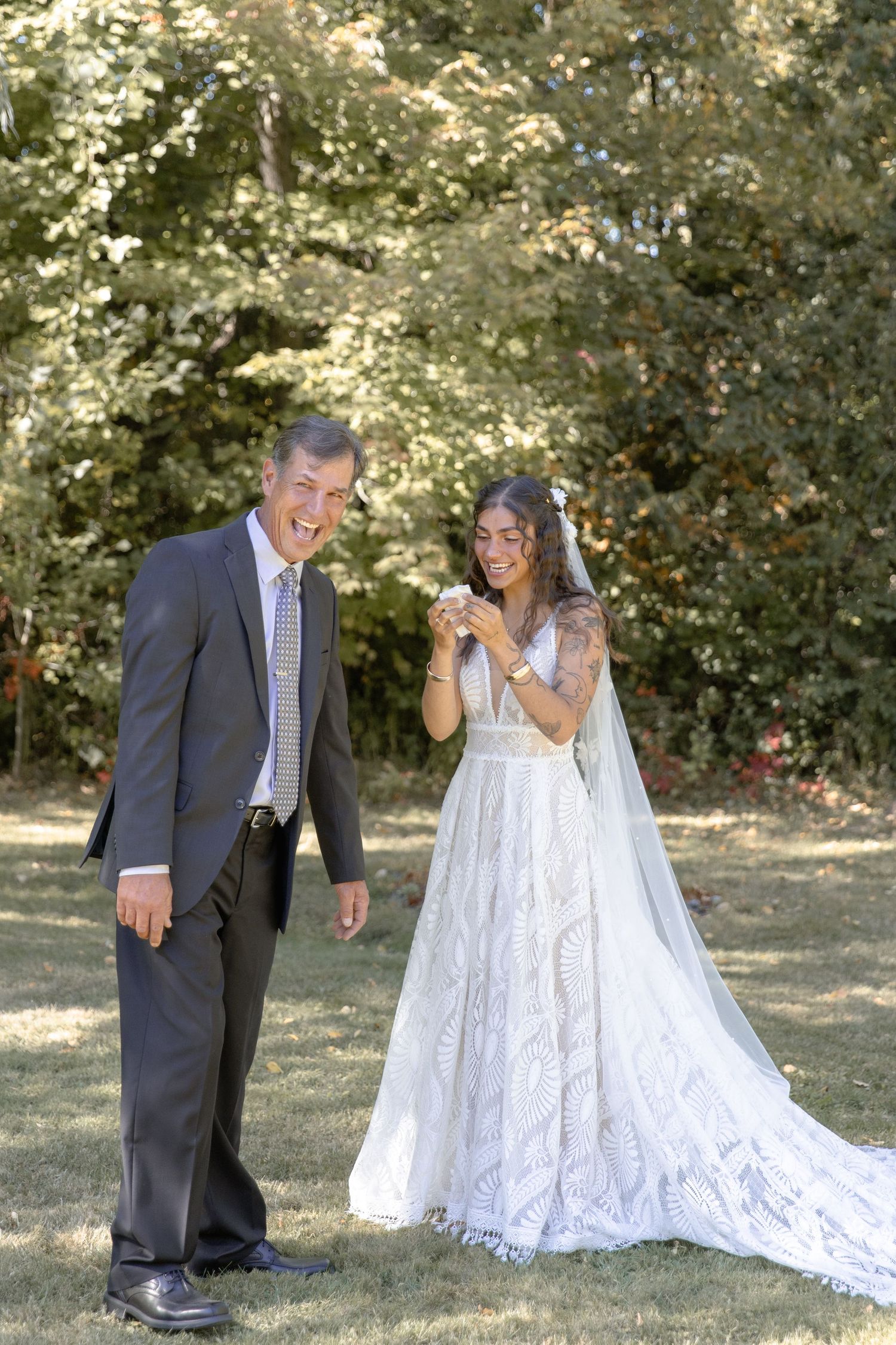 A joyful couple shares a candid moment outdoors during their wedding, with the bride wearing a lace gown and veil.