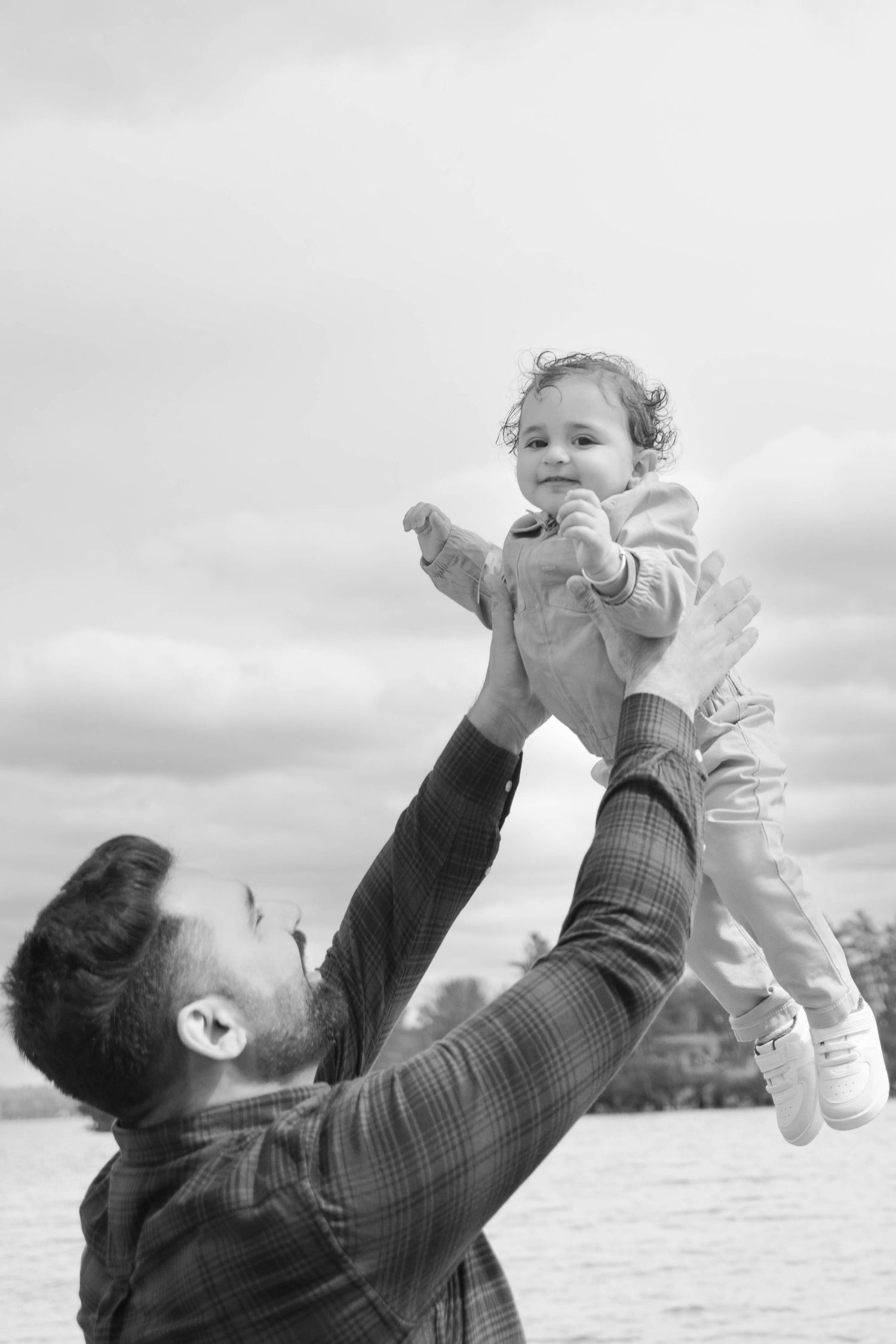 Black and white photo of a caring moment shared between parent and child playing outdoors against cloudy sky.