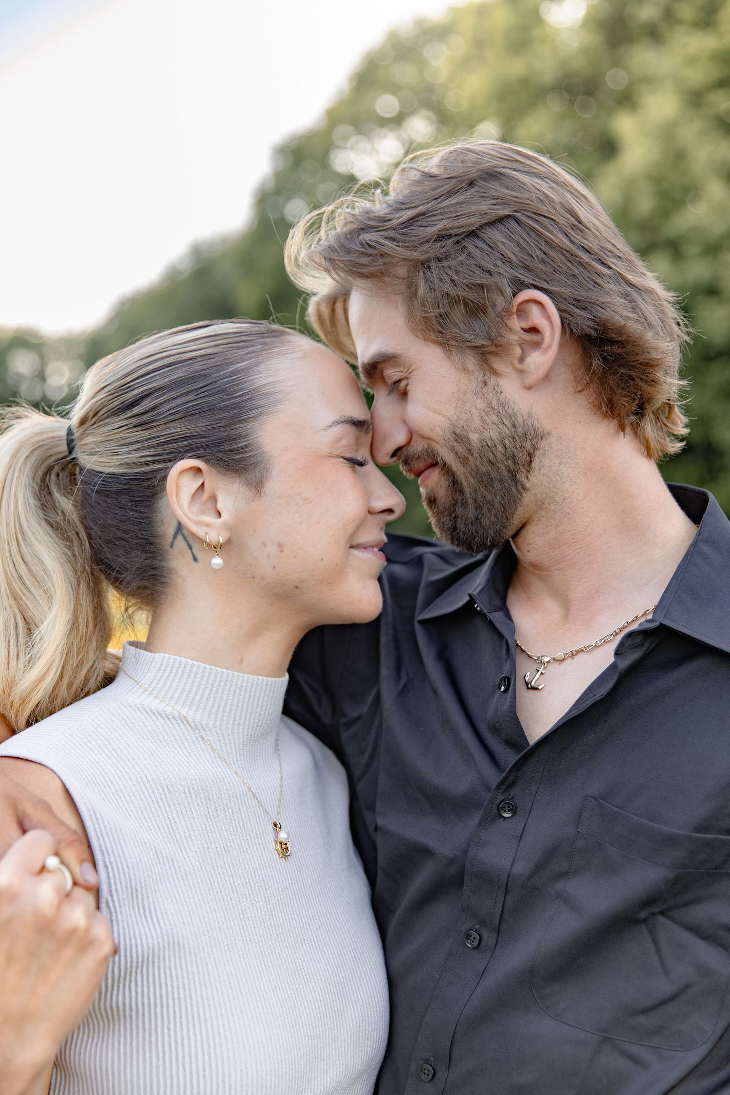 A romantic couple in black and beige outfits share tender moments in a series of four connected outdoor photos.