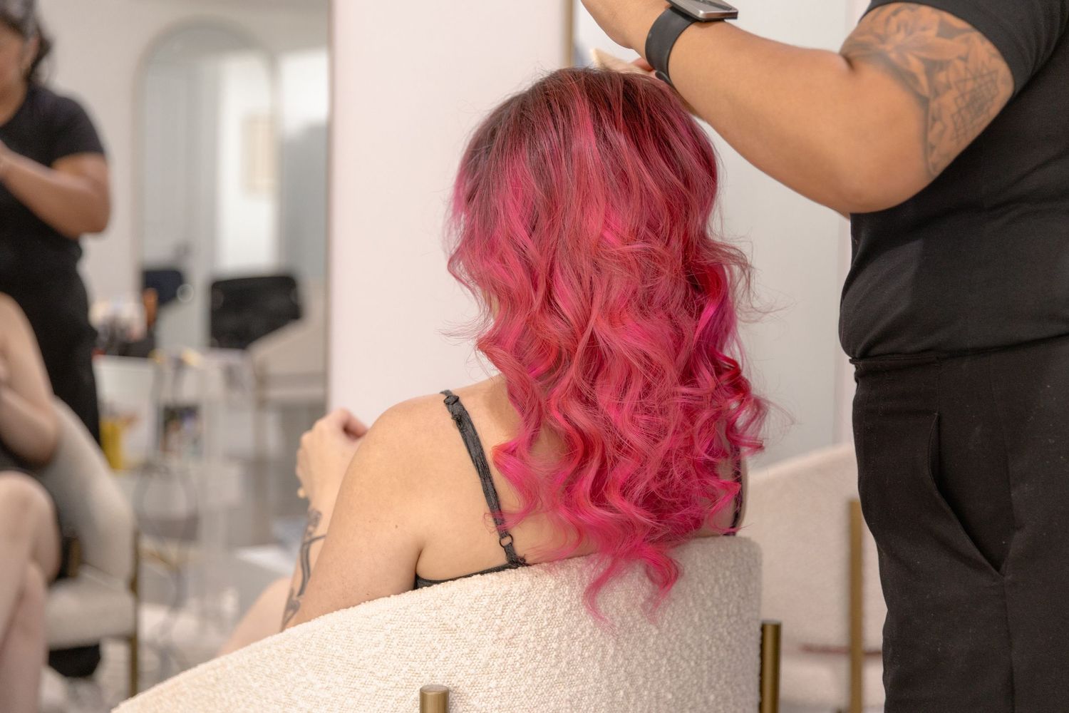 Hairstylist styling vibrant pink wavy hair at a salon.
