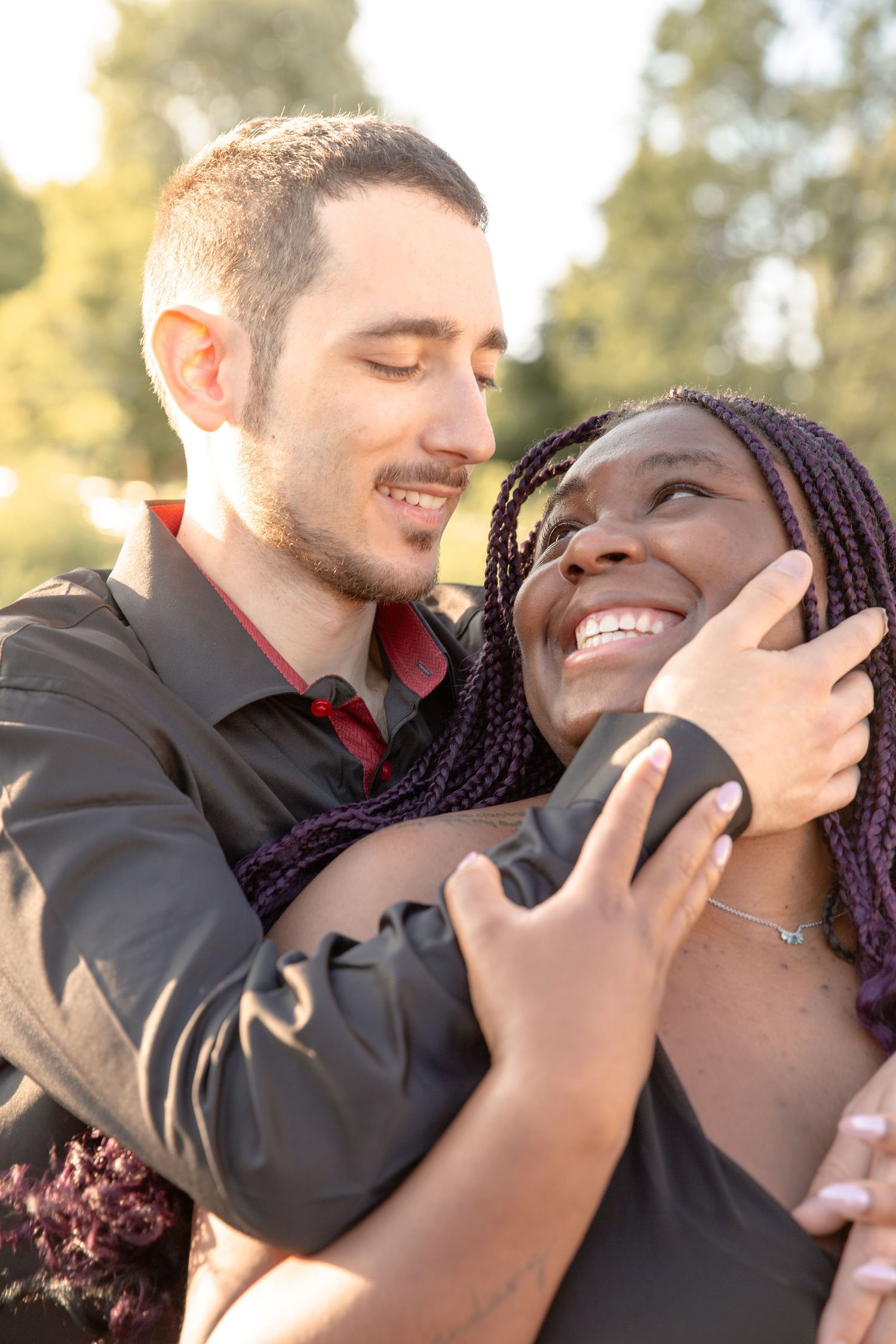 A couple shares an intimate embrace outdoors during golden hour with joyful expressions.