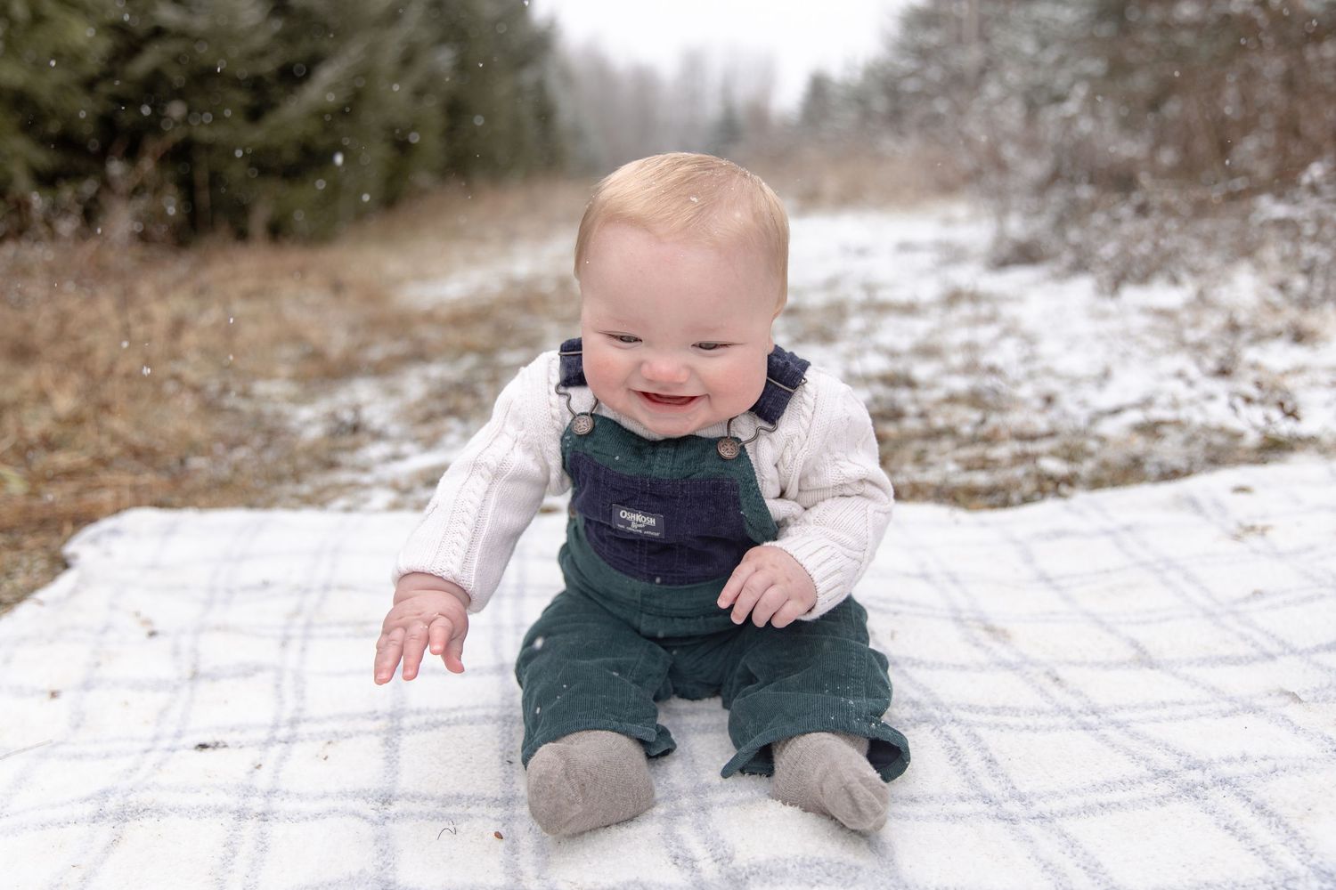 A small child in winter clothing plays in the snow while crawling across a snowy ground.